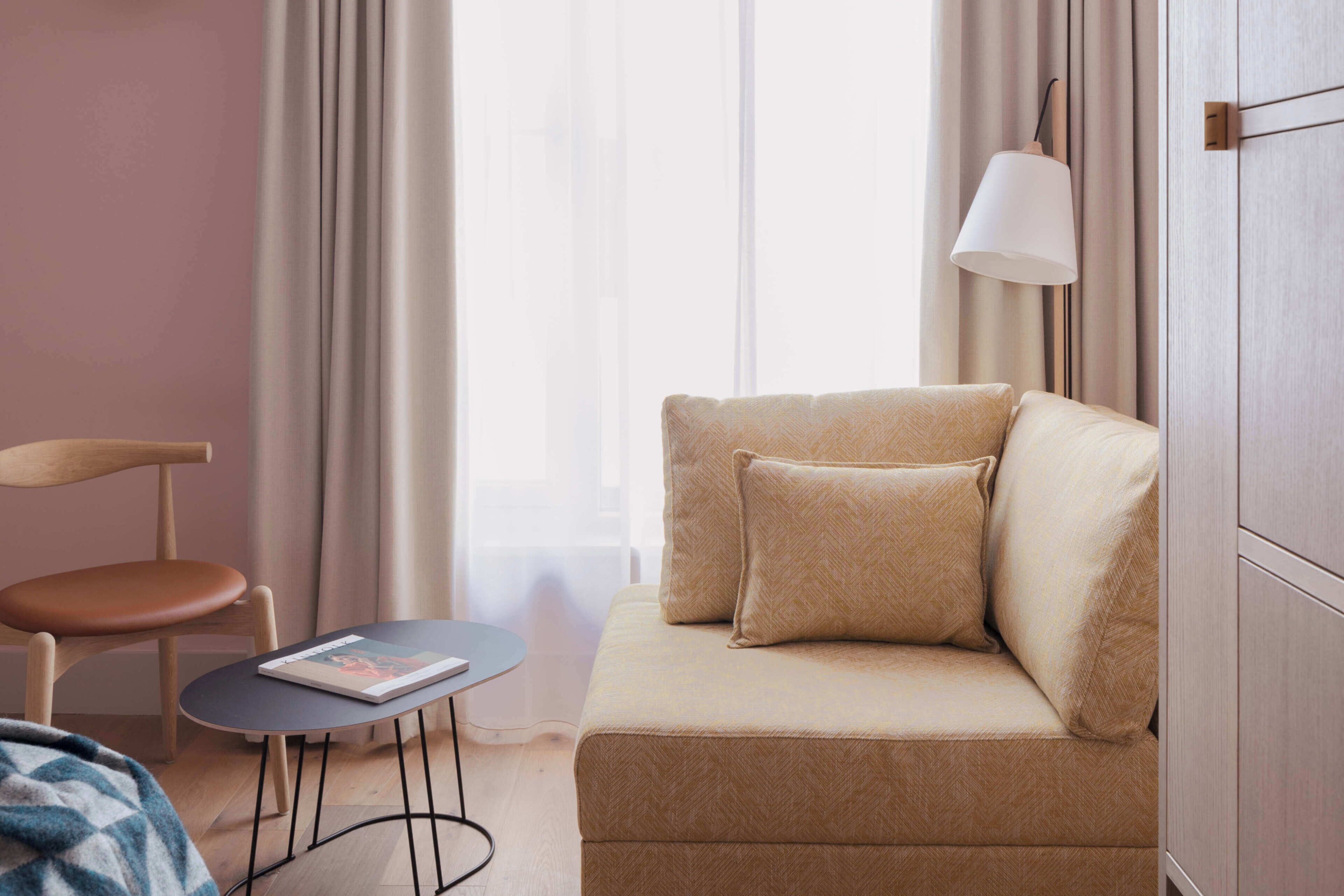 A modern hotel room with a sofa, a small table, a chair, and a lamp.