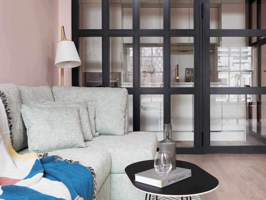 Ein modernes Wohnzimmer mit einer Couch, einem Couchtisch mit einem Buch und einem Glas sowie einer großen Glasdoor mit Blick.