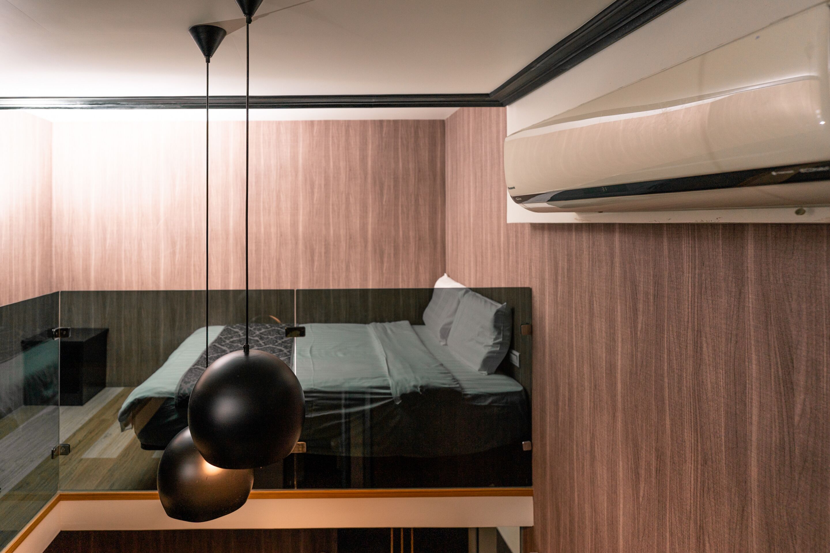 A modern bedroom with a glass partition, a bed, and a hanging light fixture.