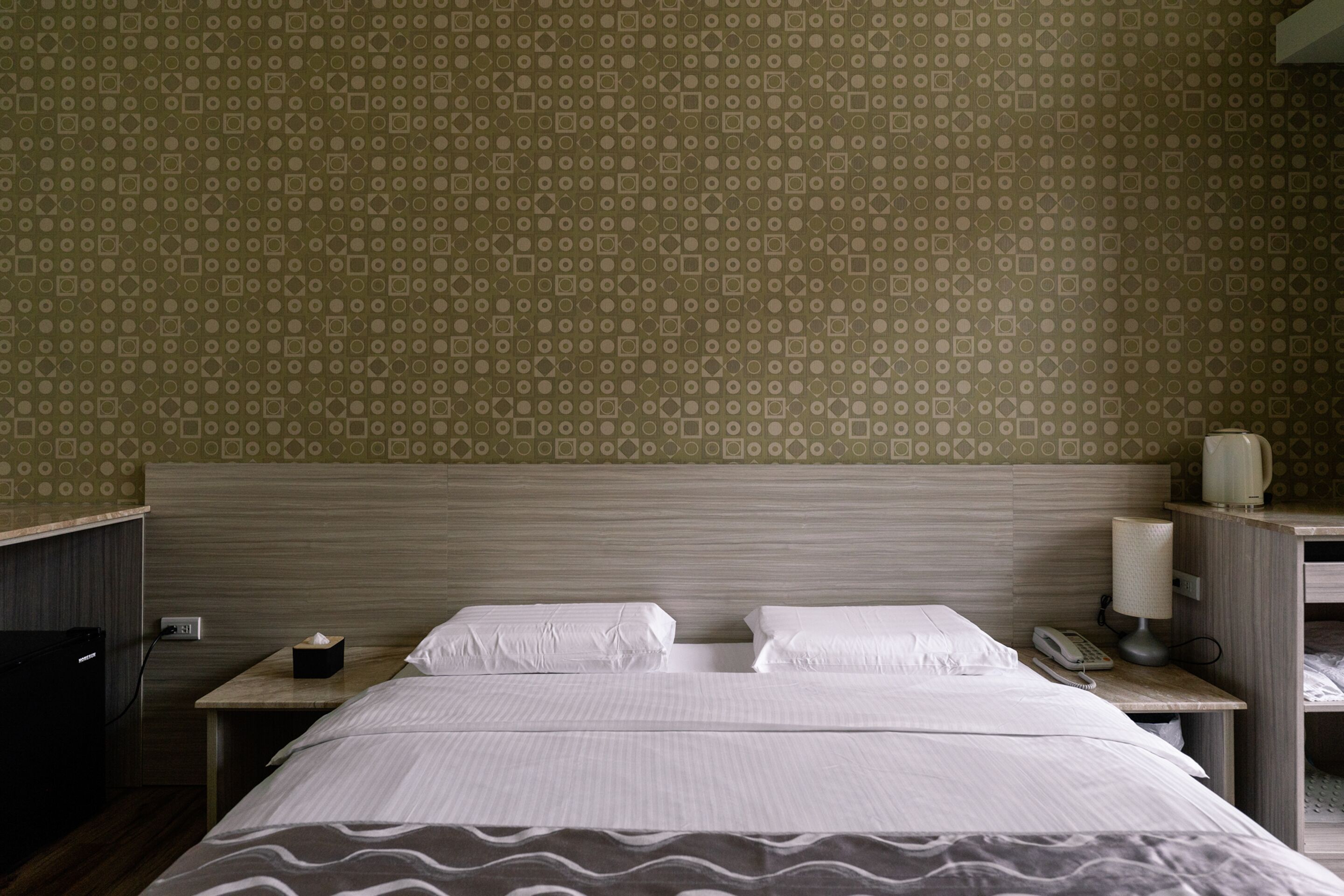 A hotel room with a bed, bedside tables, a lamp, and a telephone.