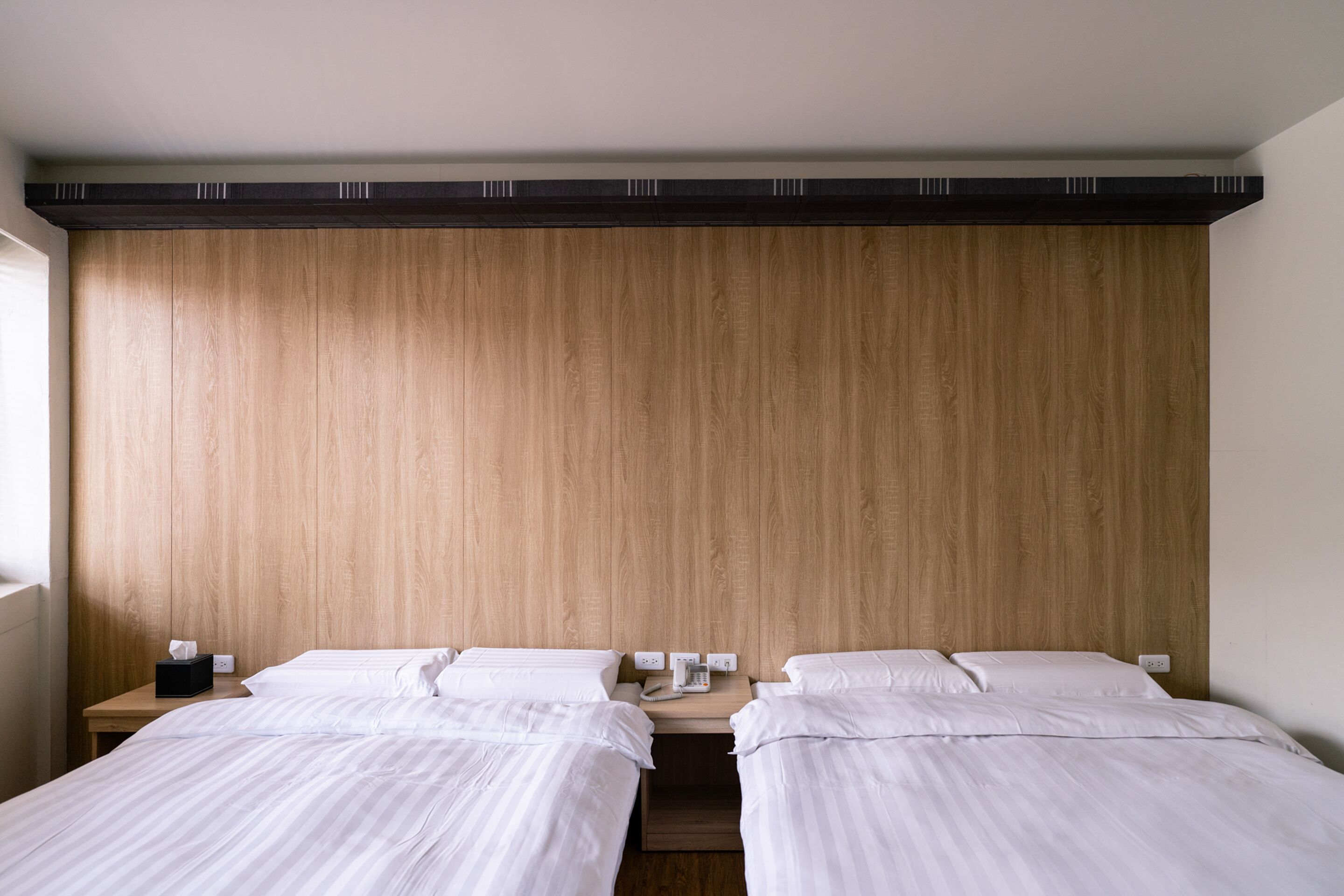 A hotel room with two beds, a wooden headboard, and a nightstand with a phone and tissues.