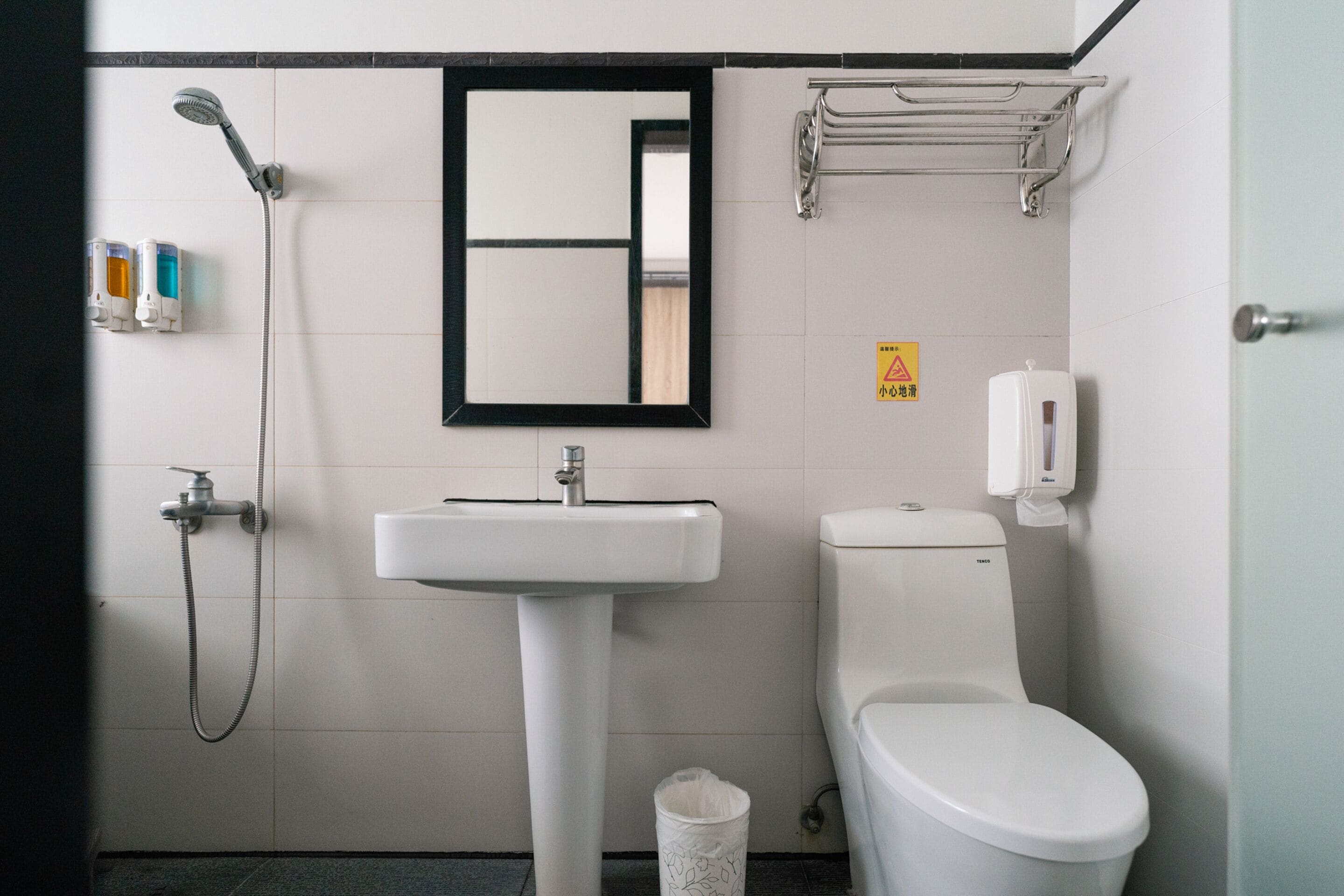 A bathroom with a white sink, a toilet, a showerhead, and a towel rack.
