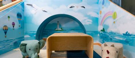 A play area with a wooden table, two animal figures, and a mural with hot air balloons, a lighthouse, and seagulls.
