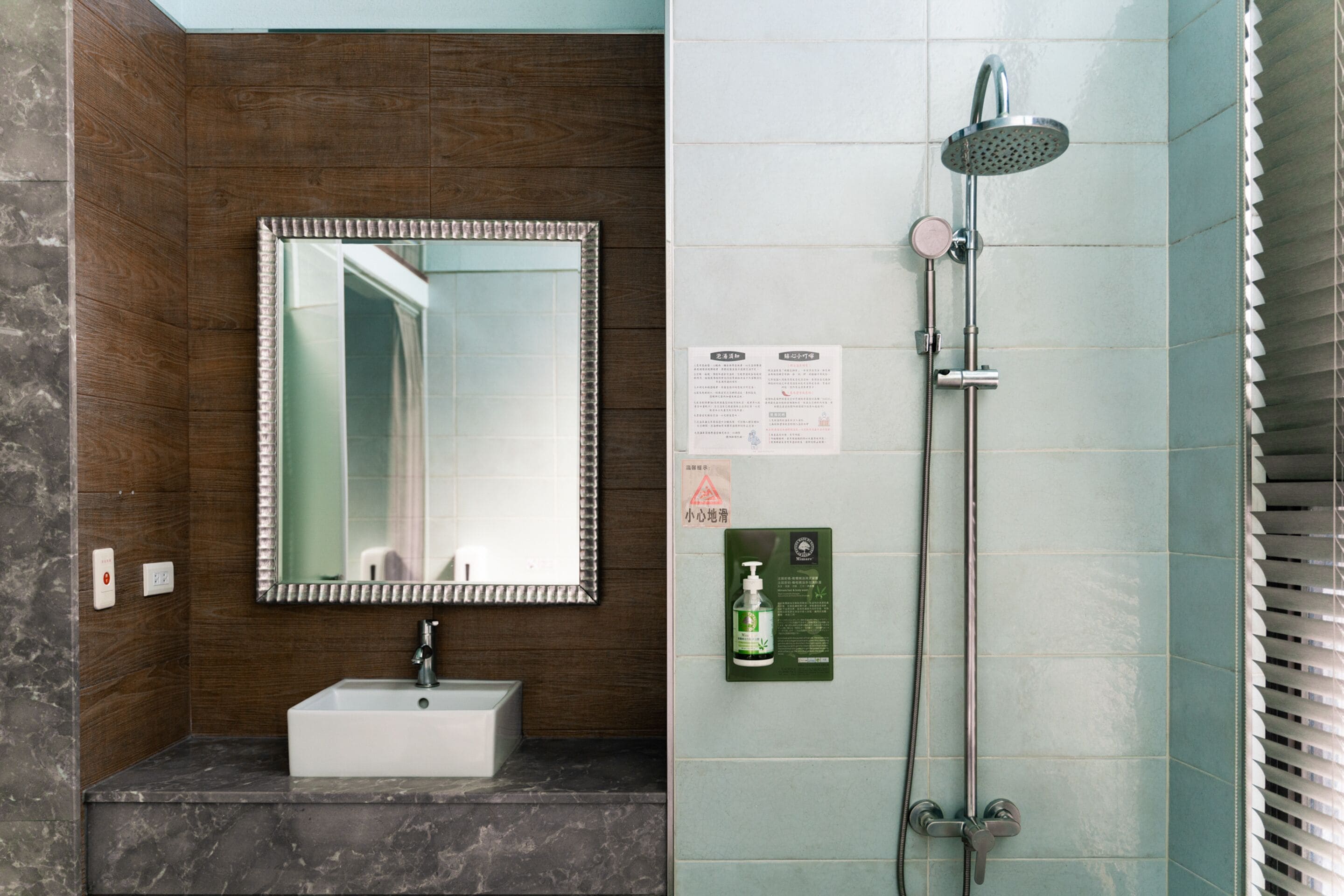 A bathroom with a sink, mirror, shower, and tiled walls.