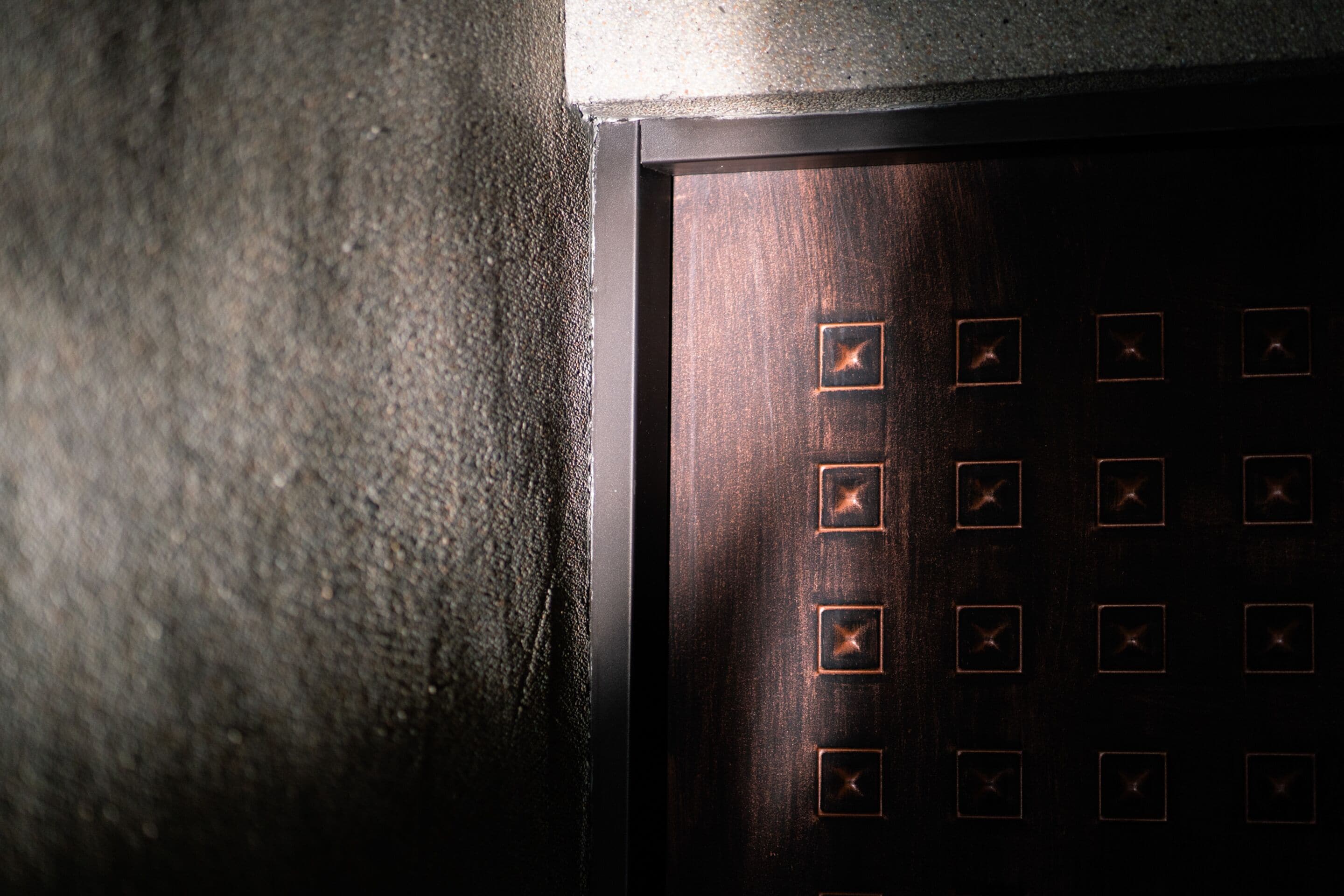 Gros plan d’une porte en bois ornée d’une série d’entailles carrées, probablement destinées à accueillir des poignées ou à servir d’éléments décoratifs.