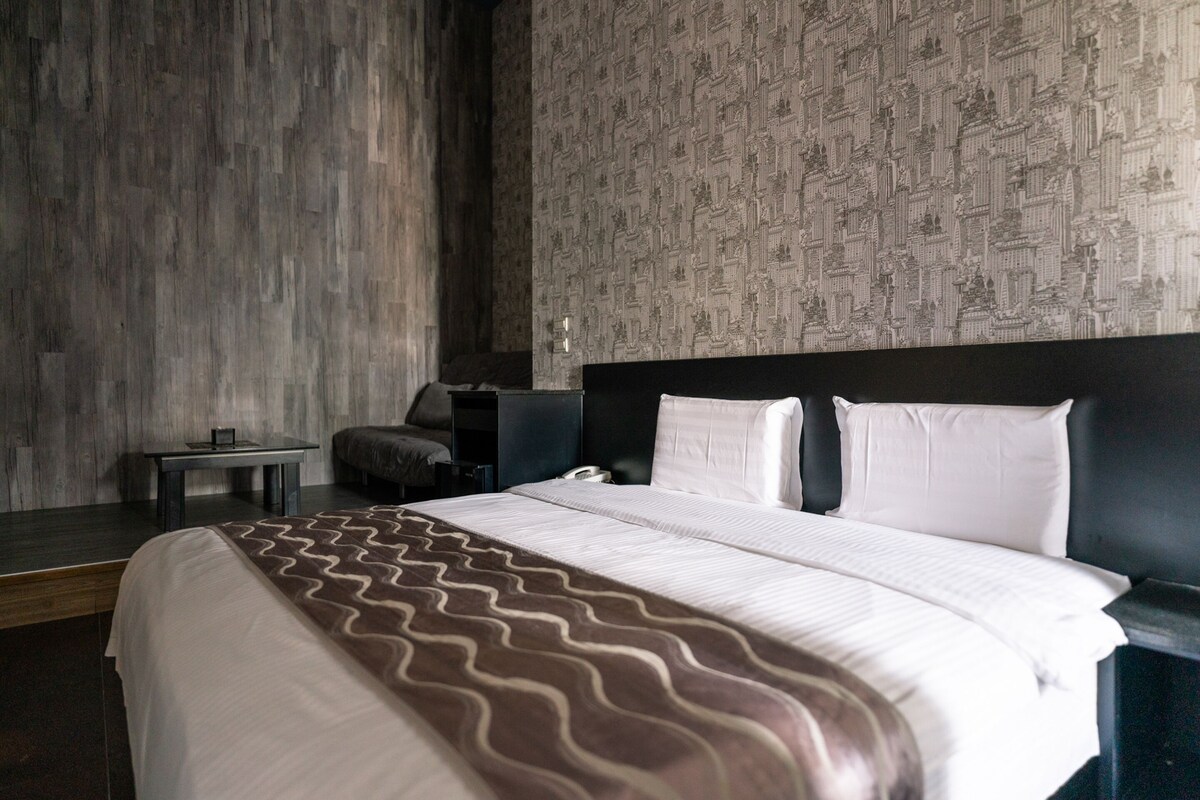 A modern hotel room with a large bed, a small side table, and a patterned wallpaper.