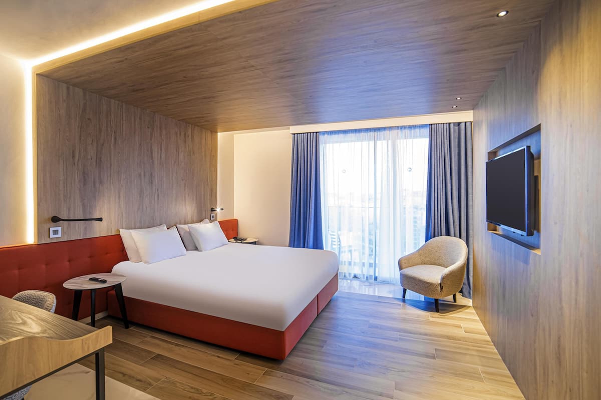 A modern hotel room with a large bed, a TV mounted on the wall, a small table, and a chair.