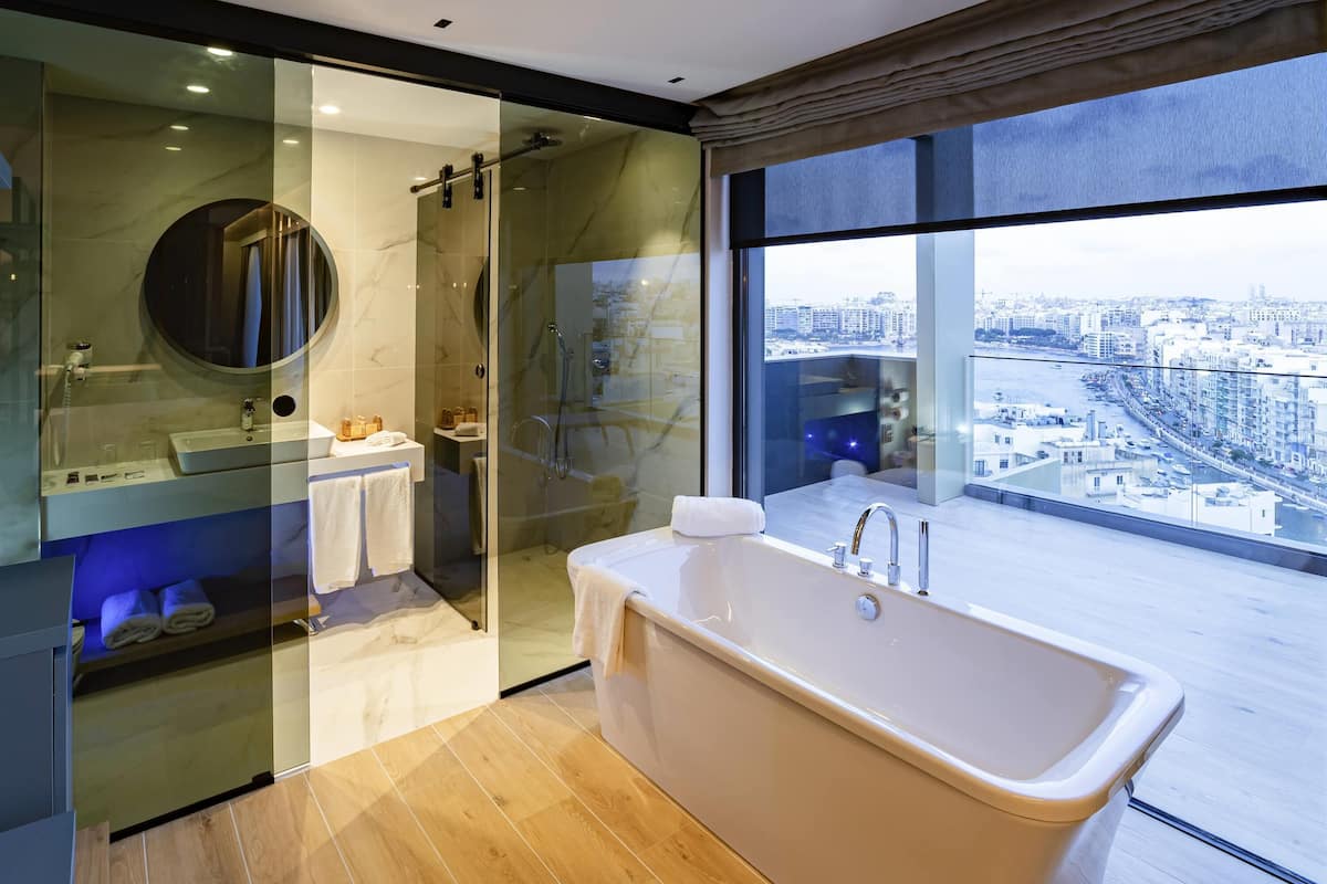 A modern bathroom with a freestanding bathtub, a glass-enclosed shower, and a large window offering a city view.