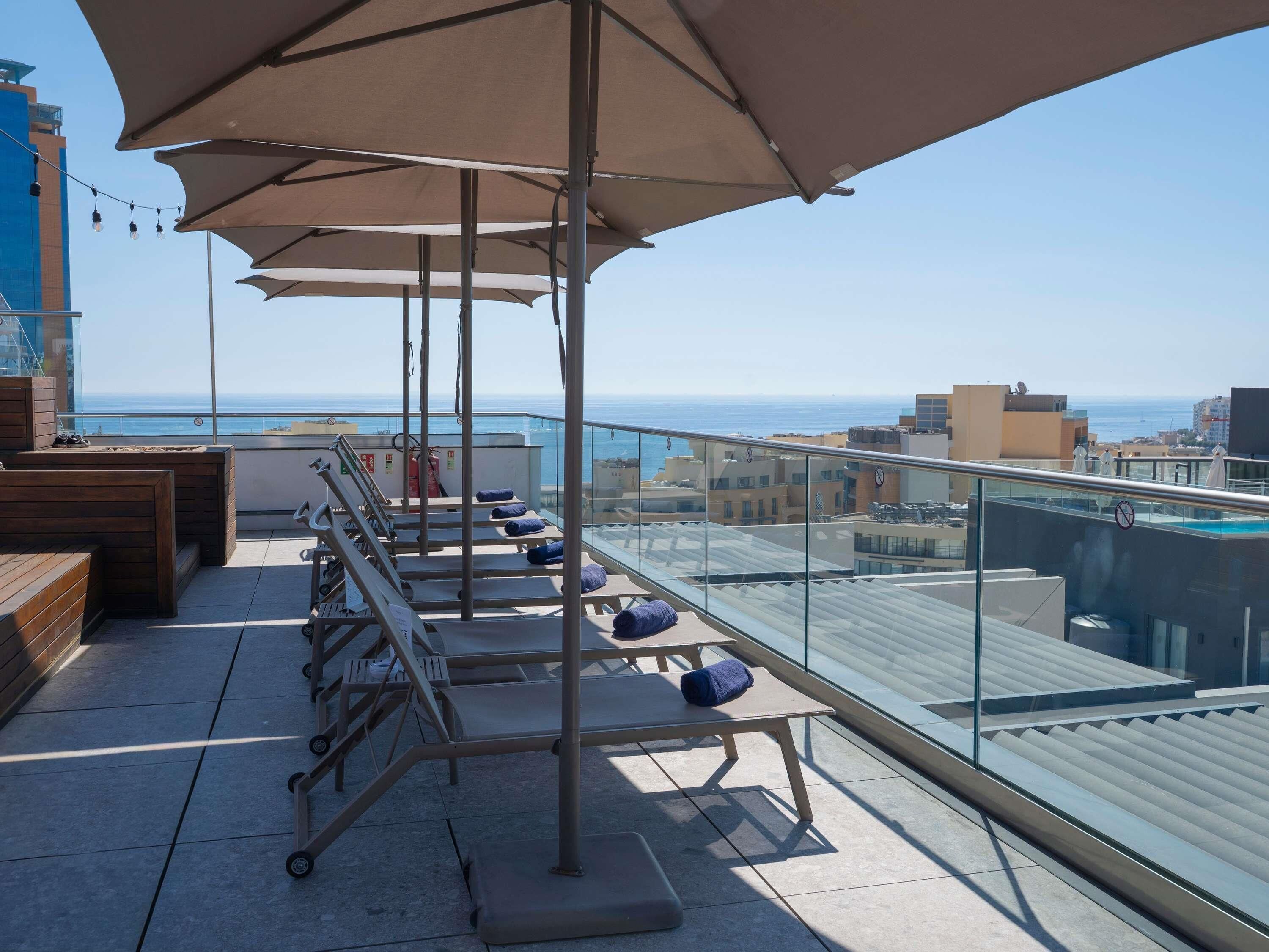 Una terraza en la azotea con sillones de sol, barandilla de cristal y vistas al mar.