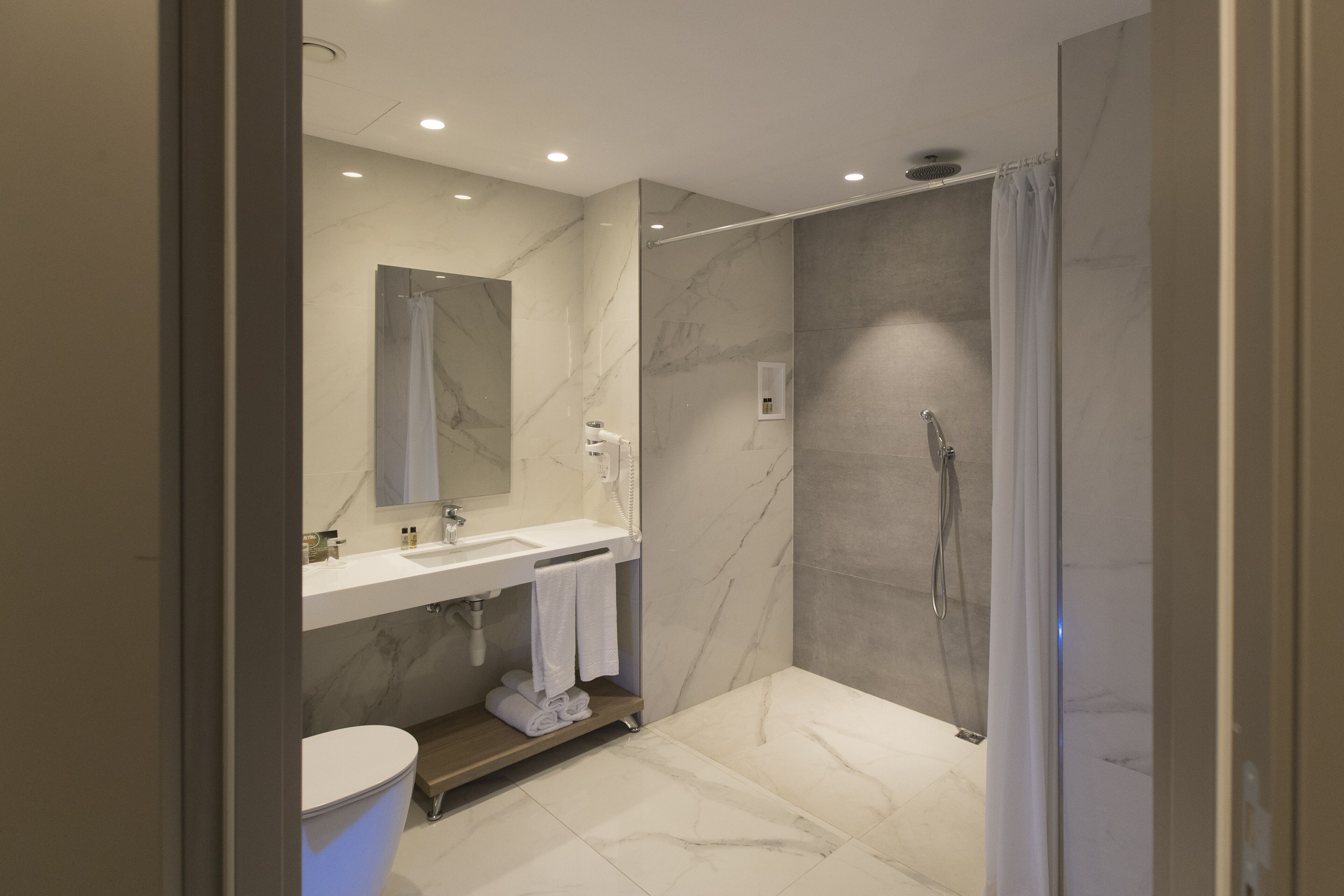 A modern bathroom with a marble shower, a white sink, and a toilet.