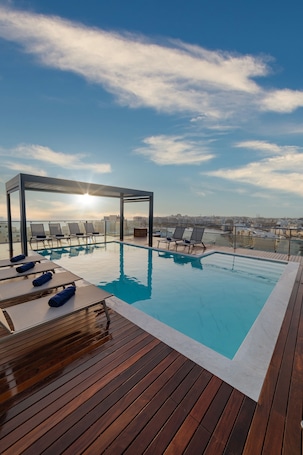 Una piscina al aire libre, sombrillas, sillones reclinables de piscina