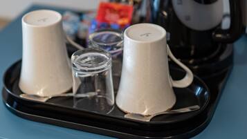 A tray with two white cups and a small glass on a blue surface, with a black kettle in the background.
