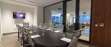 A conference room with a large table, chairs, a television, and a view of a modern interior space.