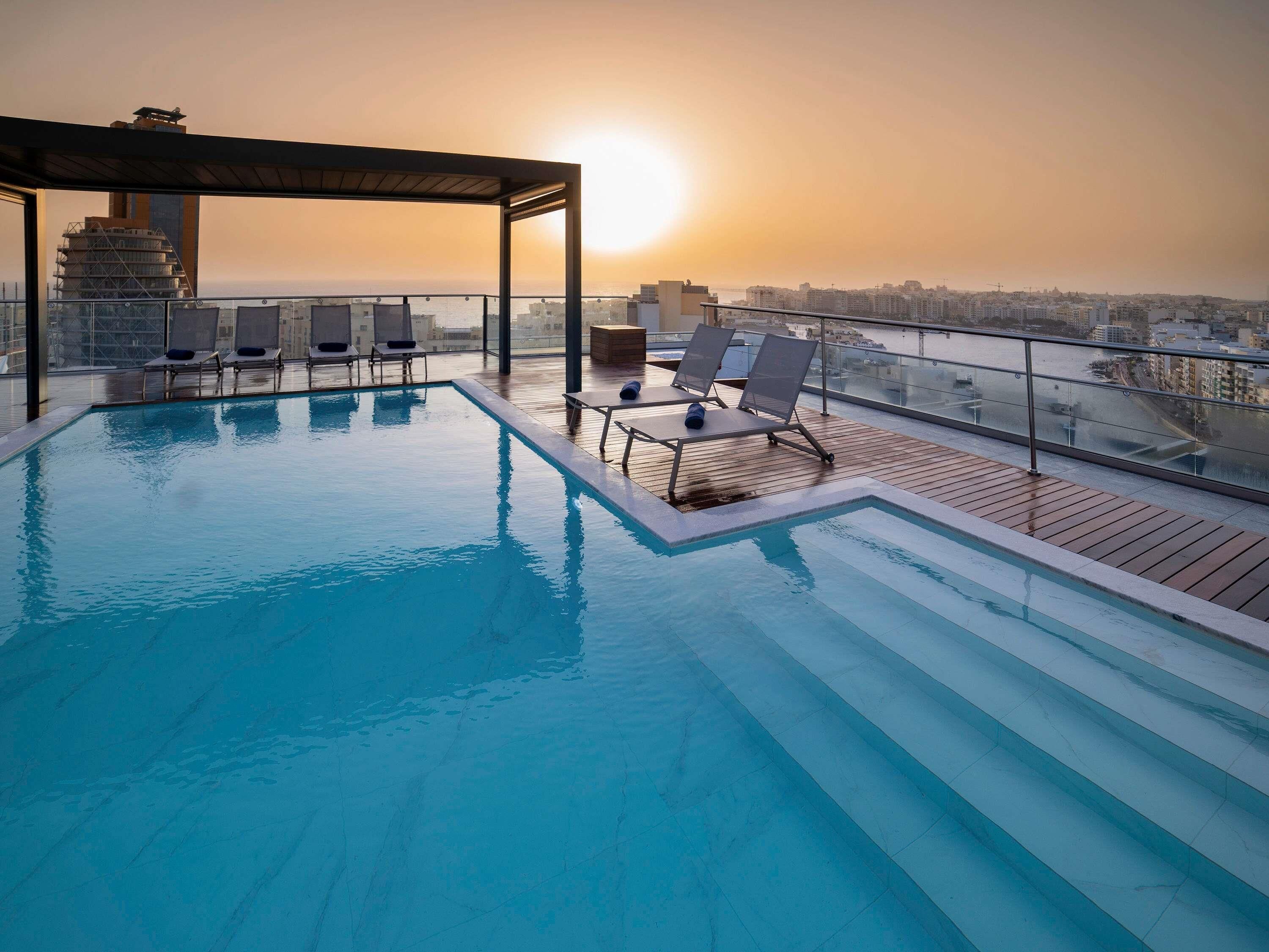 Una piscina al aire libre, sombrillas, sillones reclinables de piscina