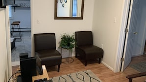 A living room with two dark brown armchairs, a small table with a laptop and remote controls, a potted plant, and a mirror on the wall. - Lilly’s Place is cozy and relaxing every room has it’s own unique style. (Glasco)