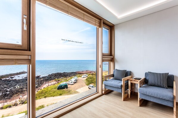 Habitación moderna con amplios ventanales que dan a una costa rocosa y coches aparcados.