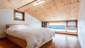 A bedroom with a wooden ceiling, a bed, and a view of the sea through large windows. - Jeju Ollero (Jeju City)