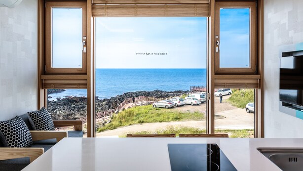 A modern room with large windows overlooking a rocky coastline and the sea. - Jeju Ollero (Jeju City)