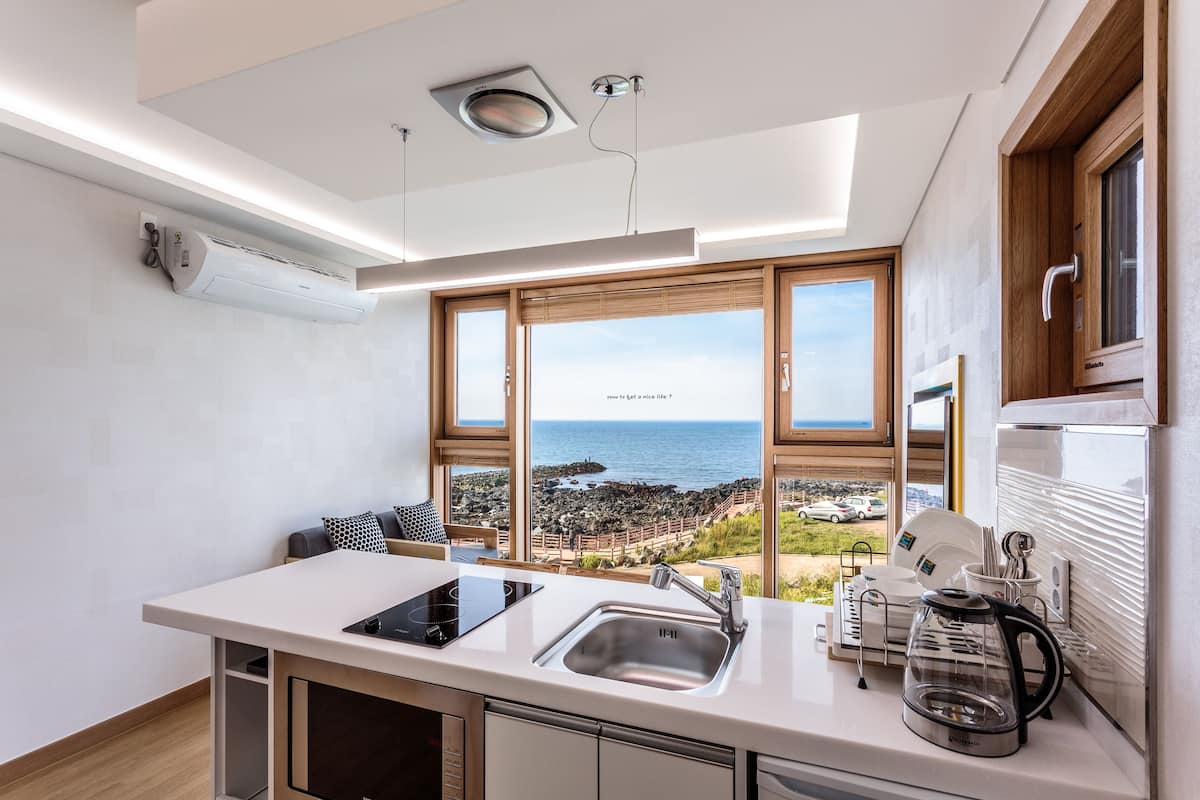 A modern kitchen with a large island, a built-in oven, and a view of the sea.