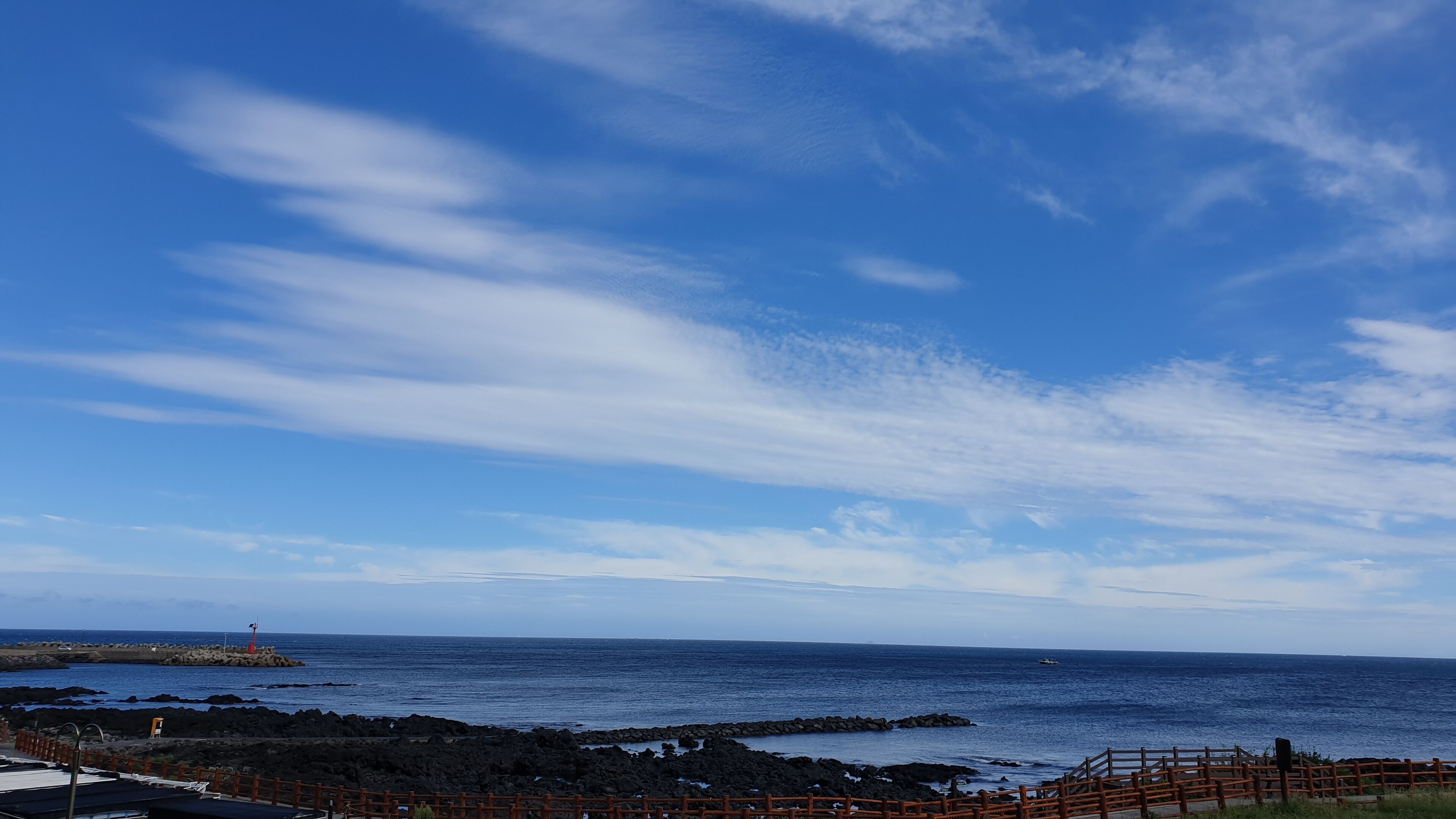 A coastal view with a clear sky, rocky shoreline, and a distant lighthouse.