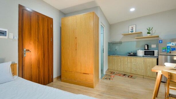 Een slaapkamer met een houten garderobe, een bed met wit beddengoed en een kleine kitchenette met een magnetron en waterkoker.