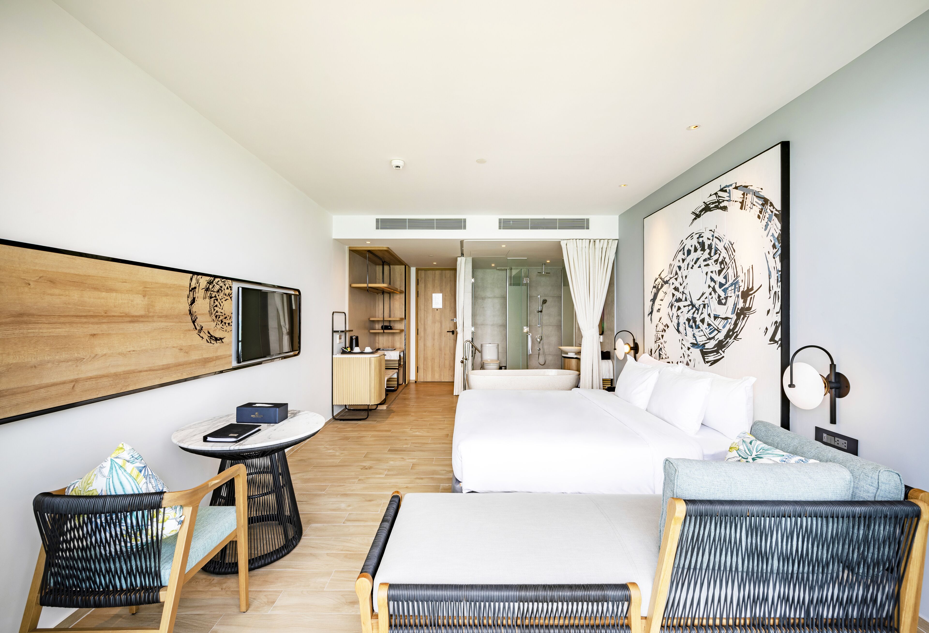 A modern hotel room with a large bed, a sofa, a dining table, and a TV.