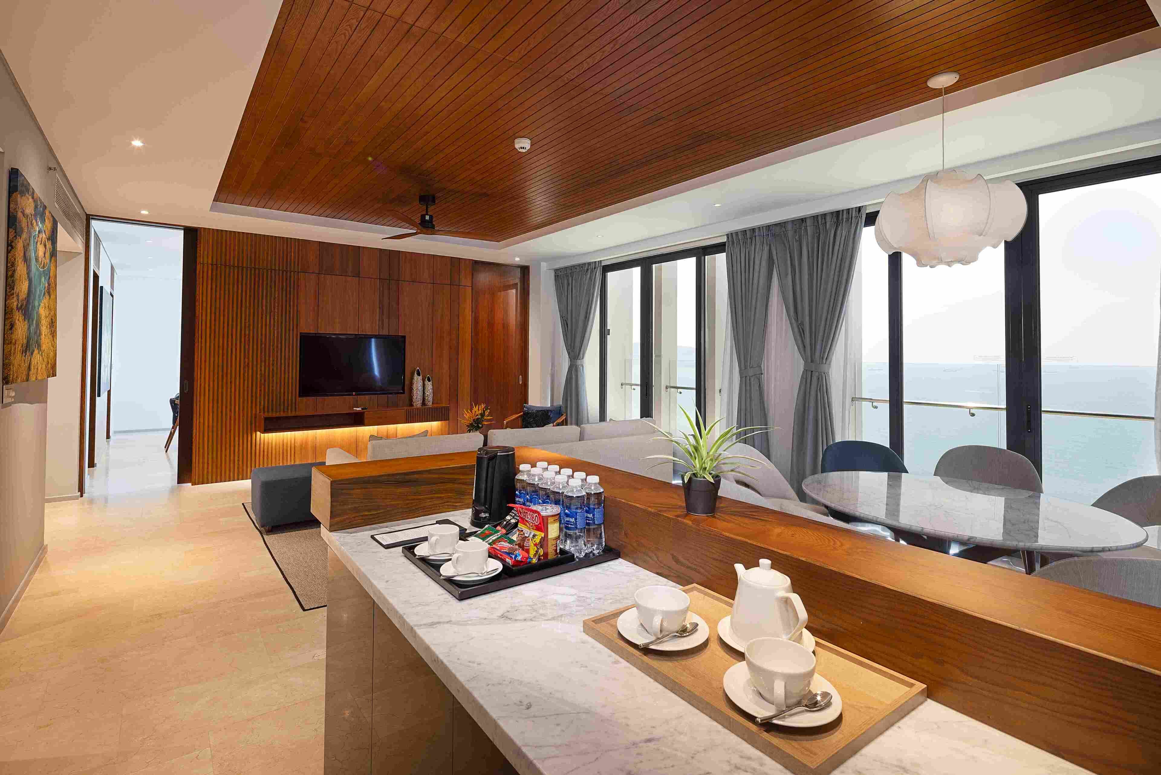 A modern hotel room with a wooden ceiling, a large TV, a dining area with a table and chairs, and a balcony with a view.