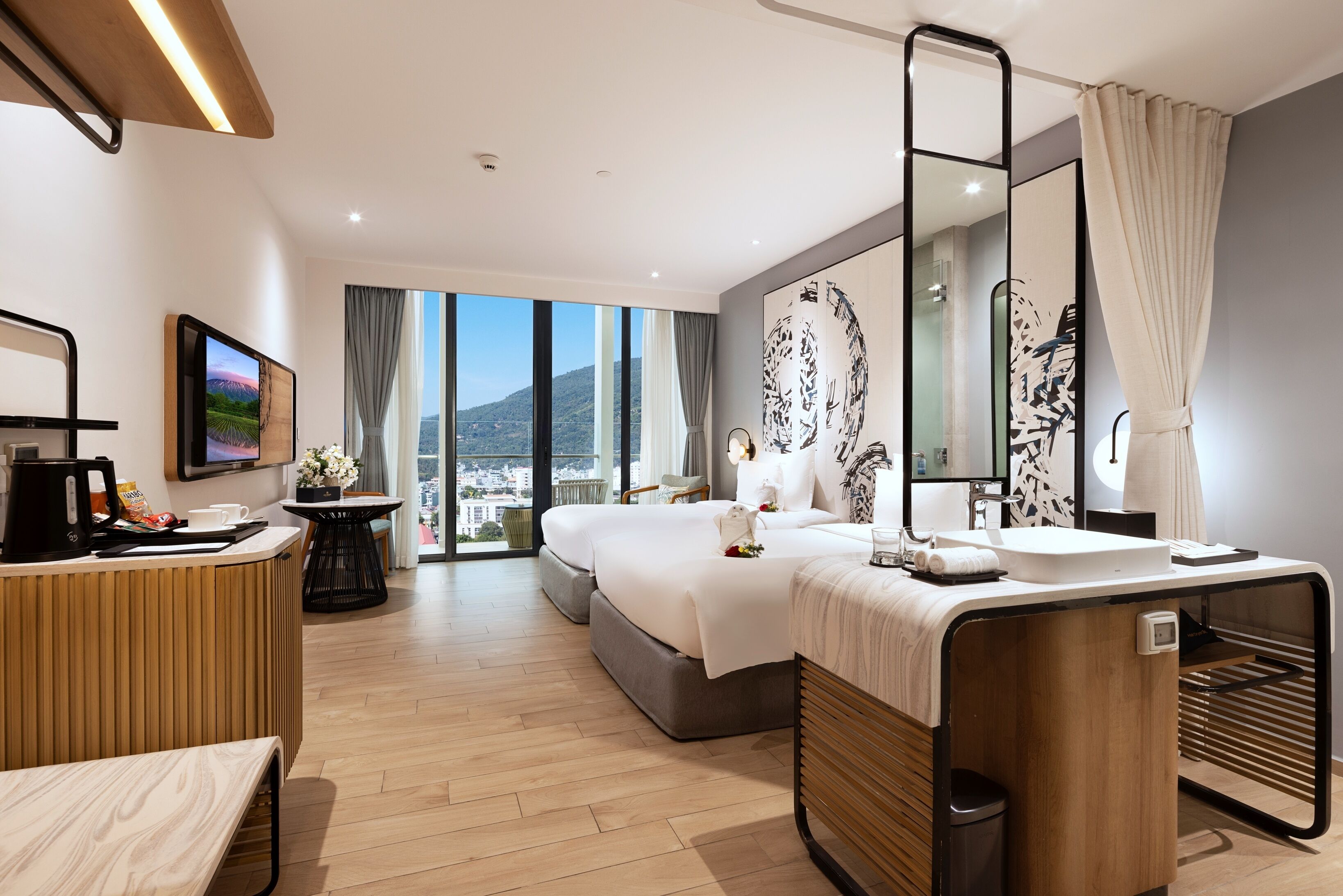 Una habitación de hotel moderna con una cama grande, un escritorio con cafetera, un baño con espejo amplio y vistas a la ciudad.