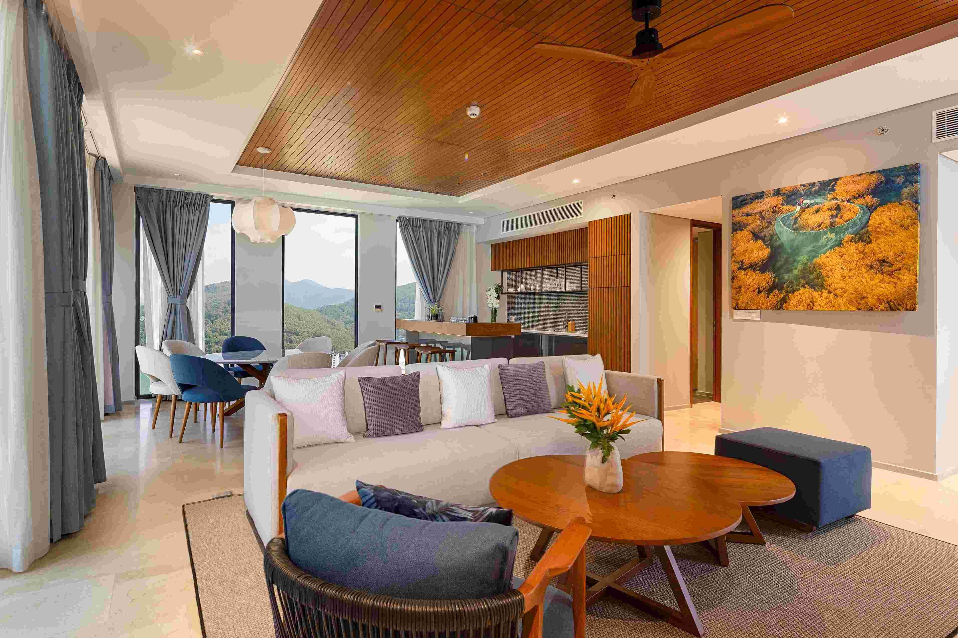 A modern living room with a sofa, coffee table, and chairs. There is a dining area with a table and chairs. A large painting is on the wall.