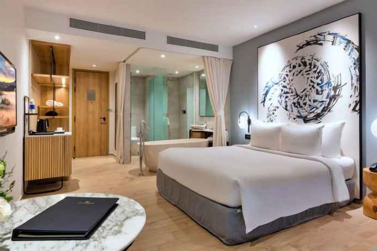 Une chambre d’hôtel moderne, dotée d’un grand lit, d’un bureau et d’une salle de bain visible à travers une porte ouverte.