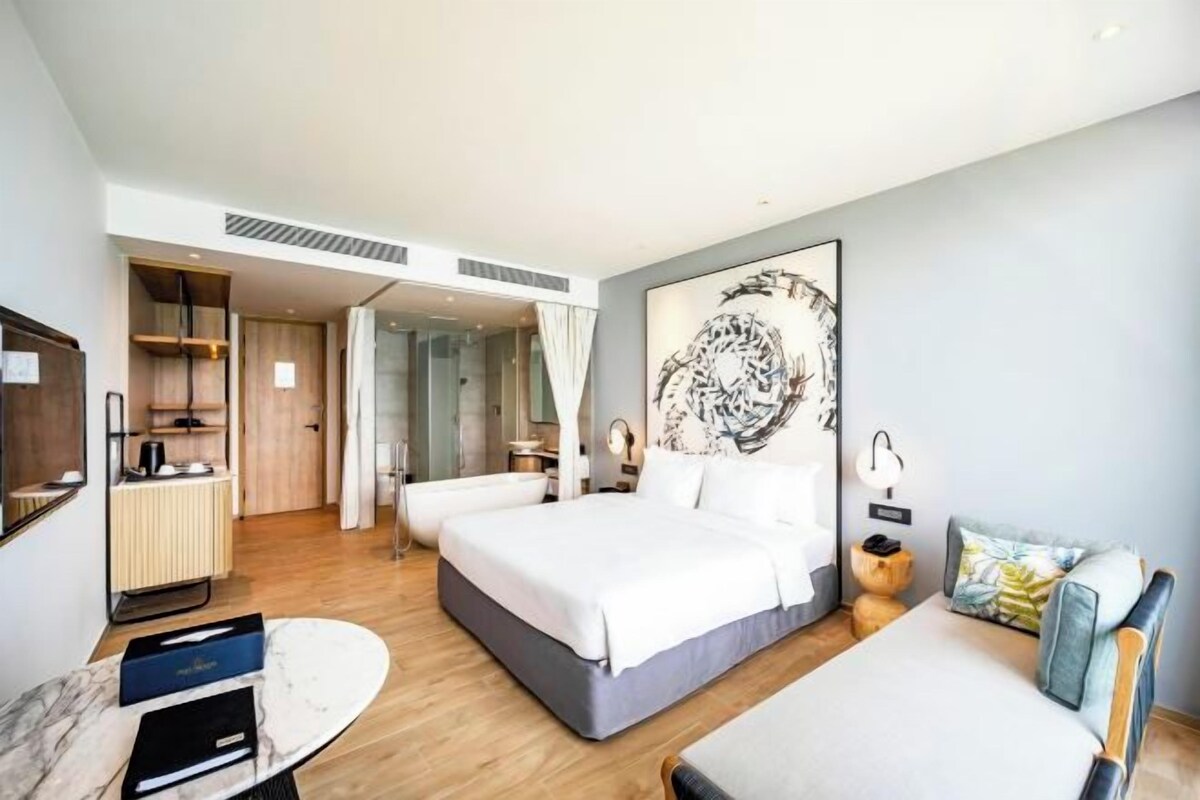 Quarto de hotel moderno com uma cama grande, uma cama menor, área de estar, toucador e uma grande pintura abstrata na parede.