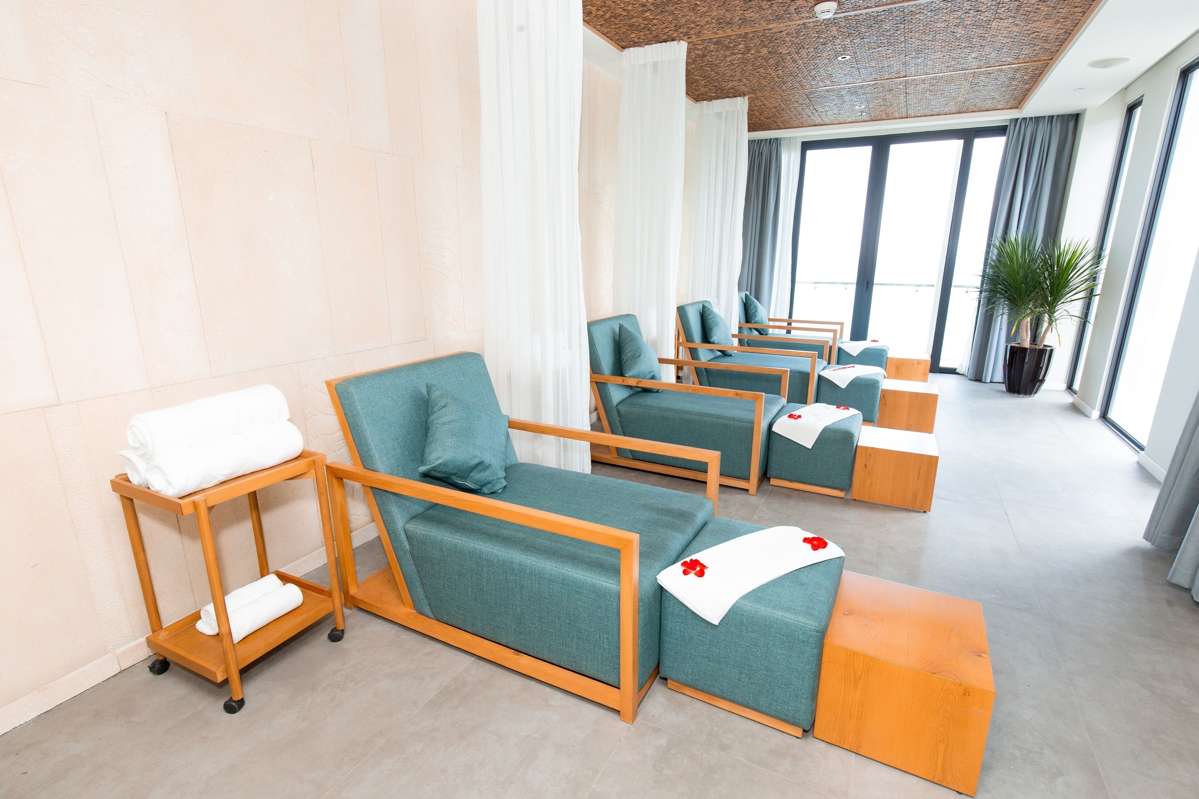 Une salle de spa moderne équipée de plusieurs fauteuils de massage, d’un chariot en bois contenant des serviettes et d’une grande plante en pot.