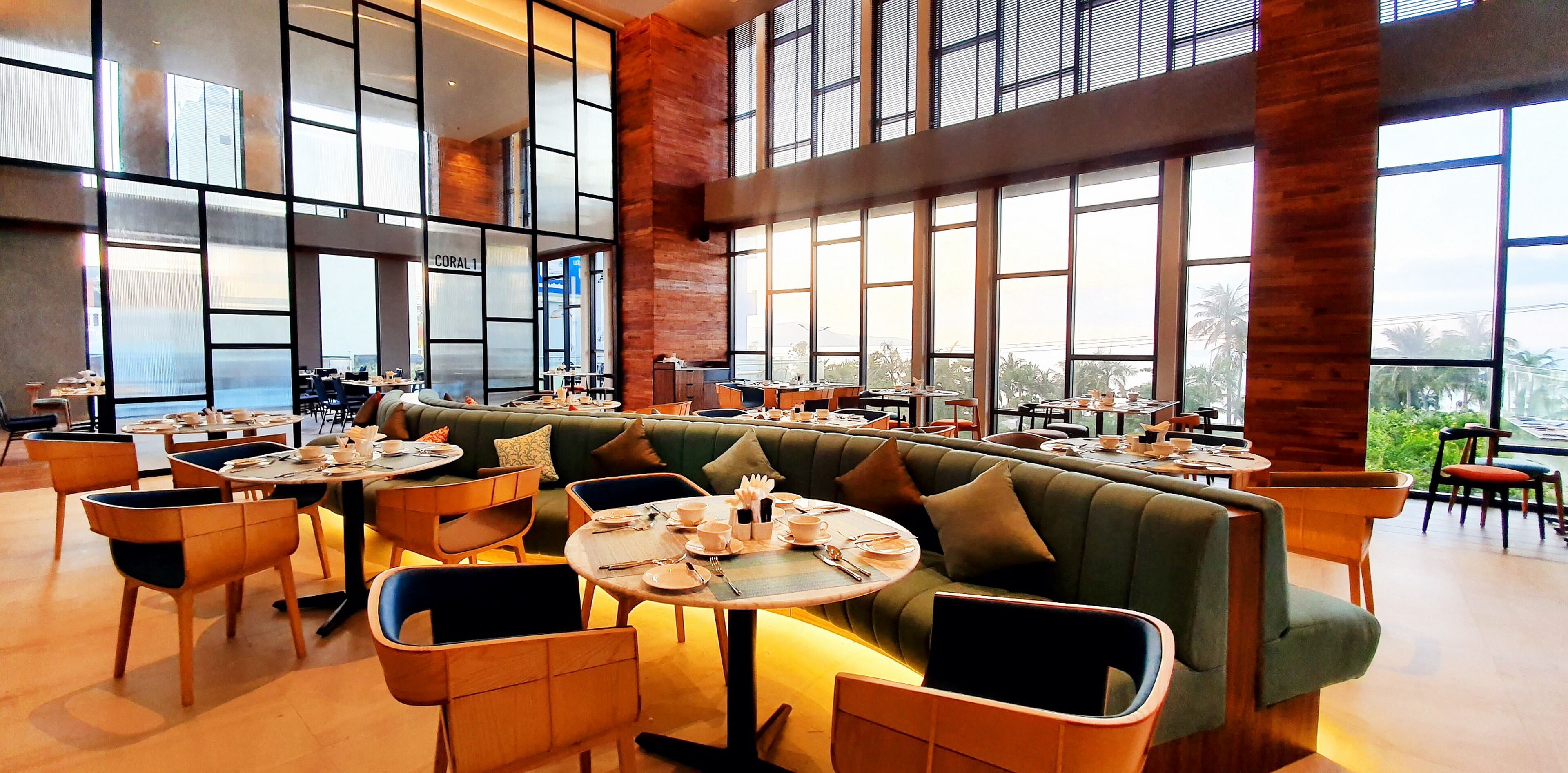 A spacious indoor dining area with high ceilings, large windows, and a central seating area with tables and chairs.