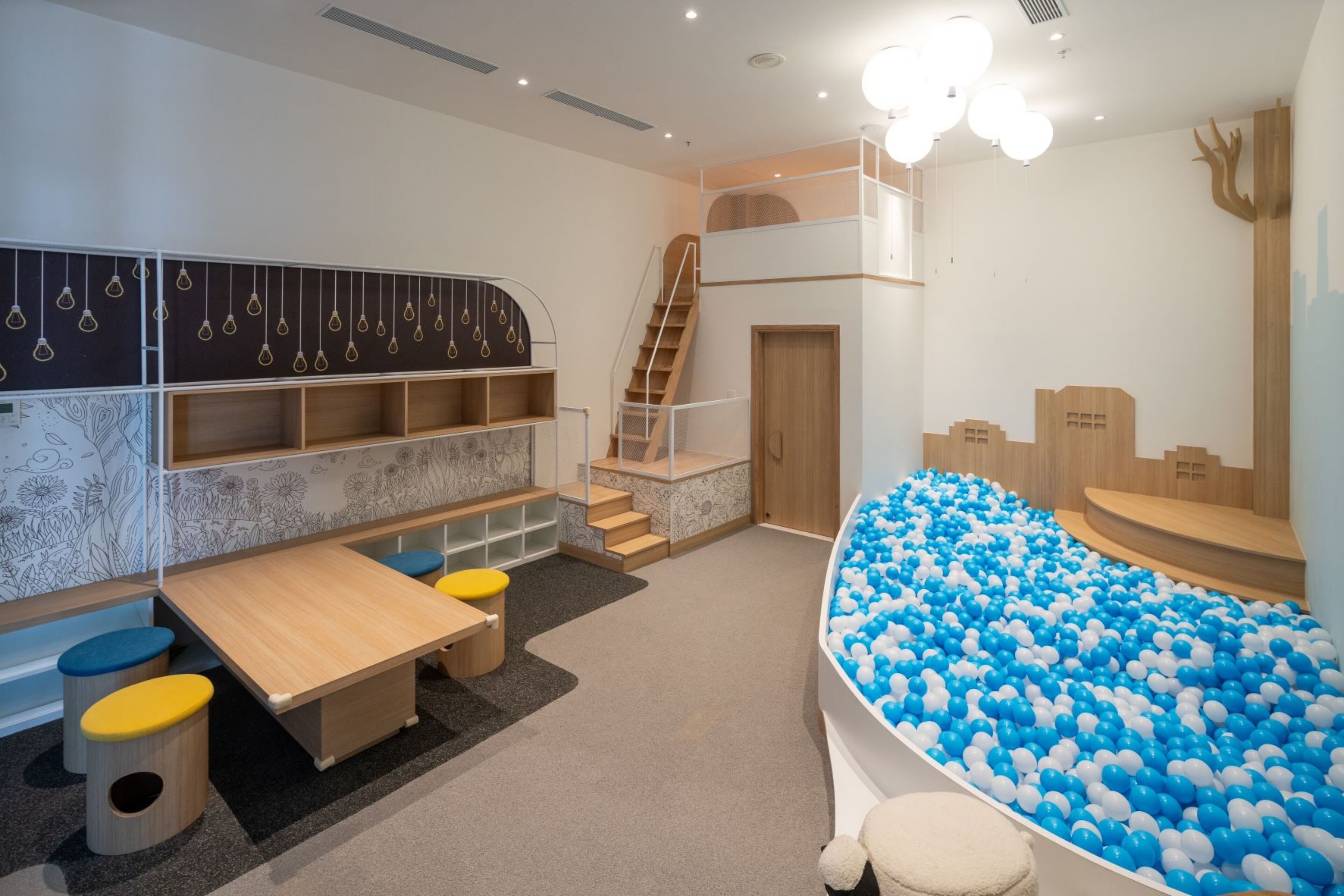 Zona de juegos infantiles con piscina de pelotas, una mesa de juego de madera y una escalera.