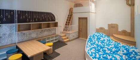 Zona de juegos infantiles con piscina de pelotas, una mesa de juego de madera y una escalera.