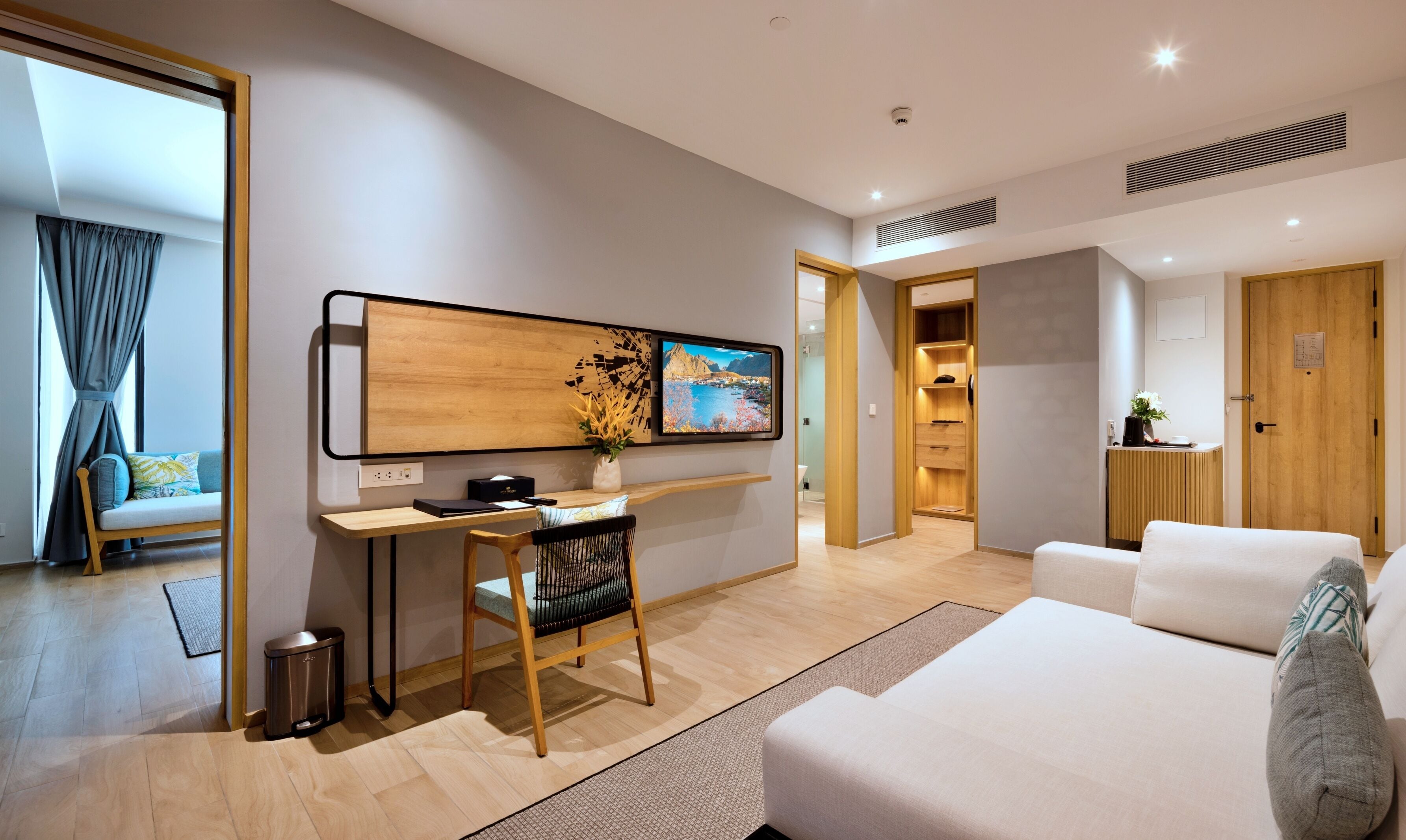 A modern hotel room with a wooden desk, a comfortable sofa, a TV mounted on the wall, and a view of the outdoors.
