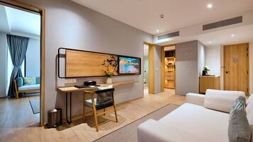A modern hotel room with a wooden desk, a comfortable sofa, a TV mounted on the wall, and a view of the outdoors.