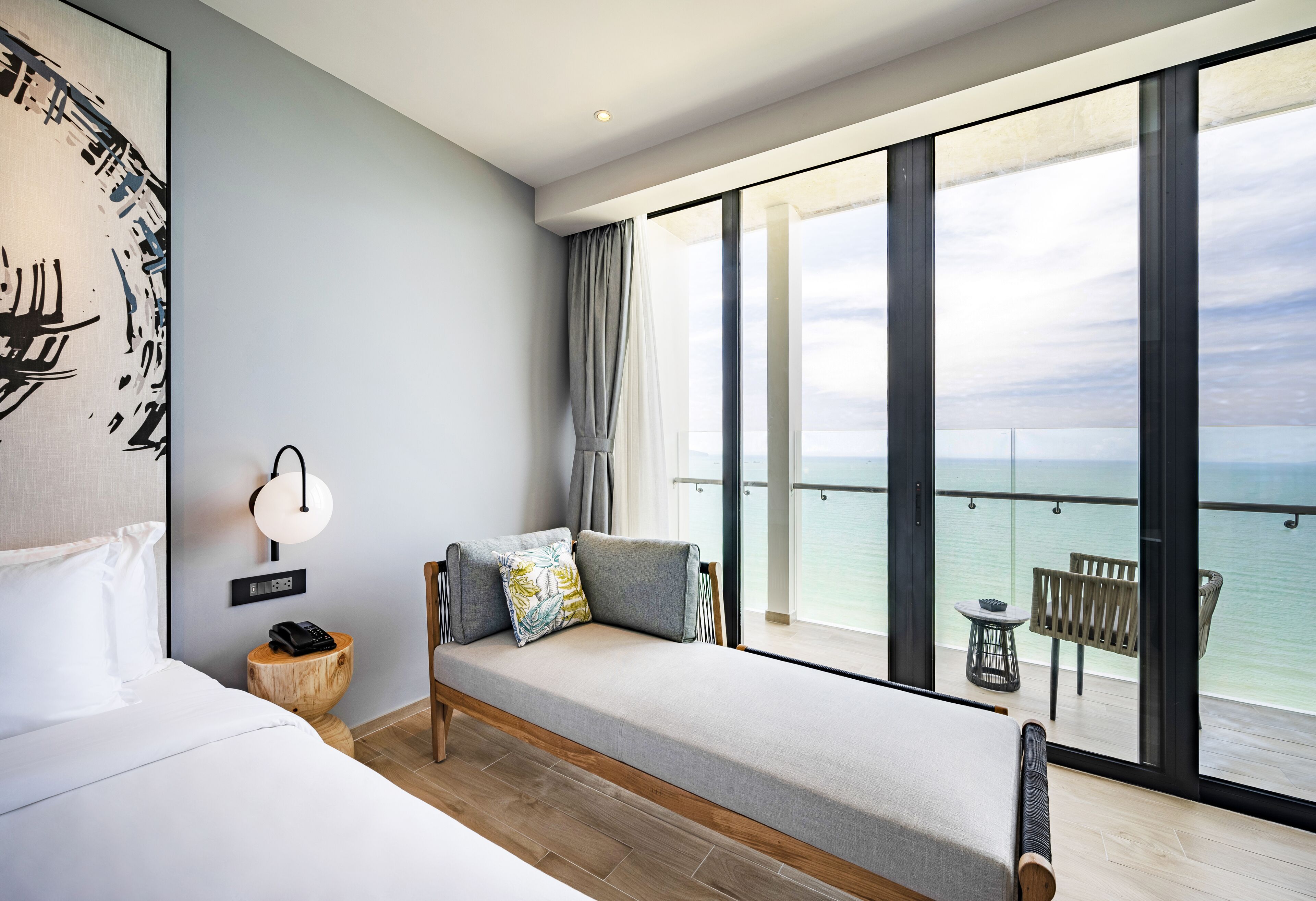 A modern hotel room with a large balcony, a bed, a sofa, and a view of the sea.