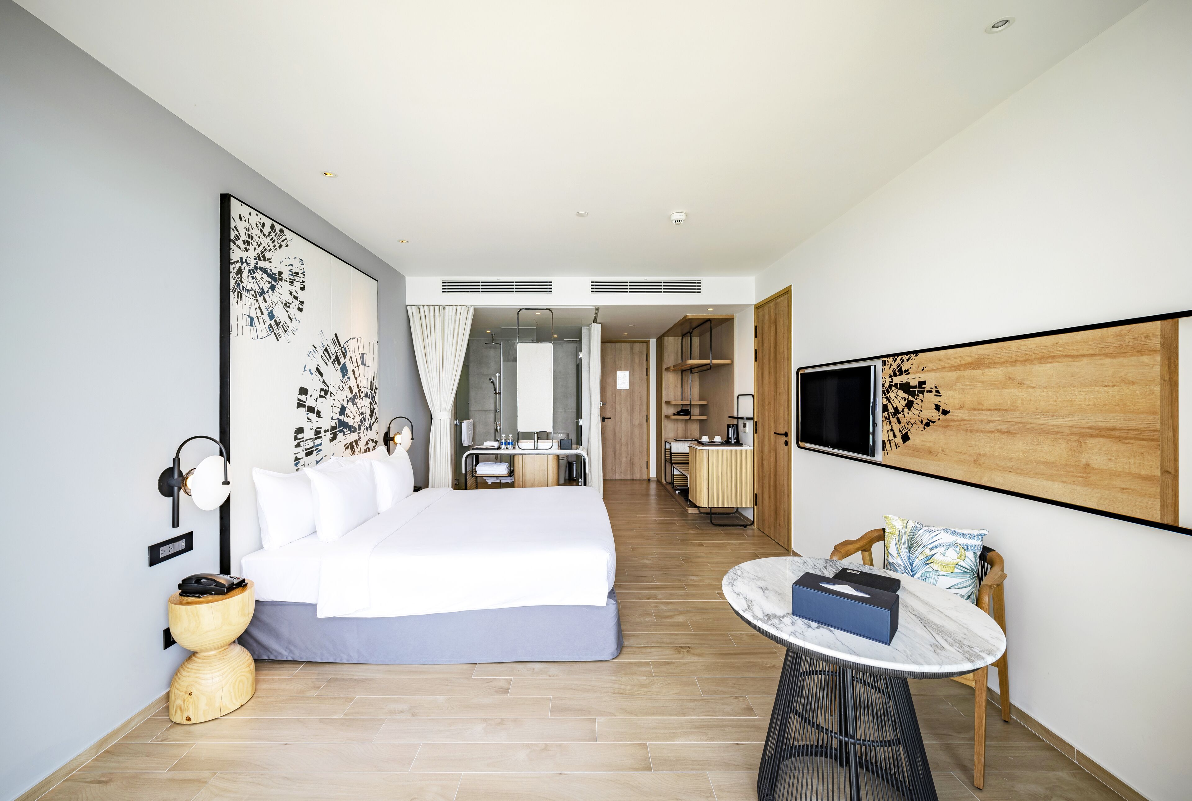 Una habitación de hotel moderna con una cama grande, una mesa redonda y un televisor montado en la pared.