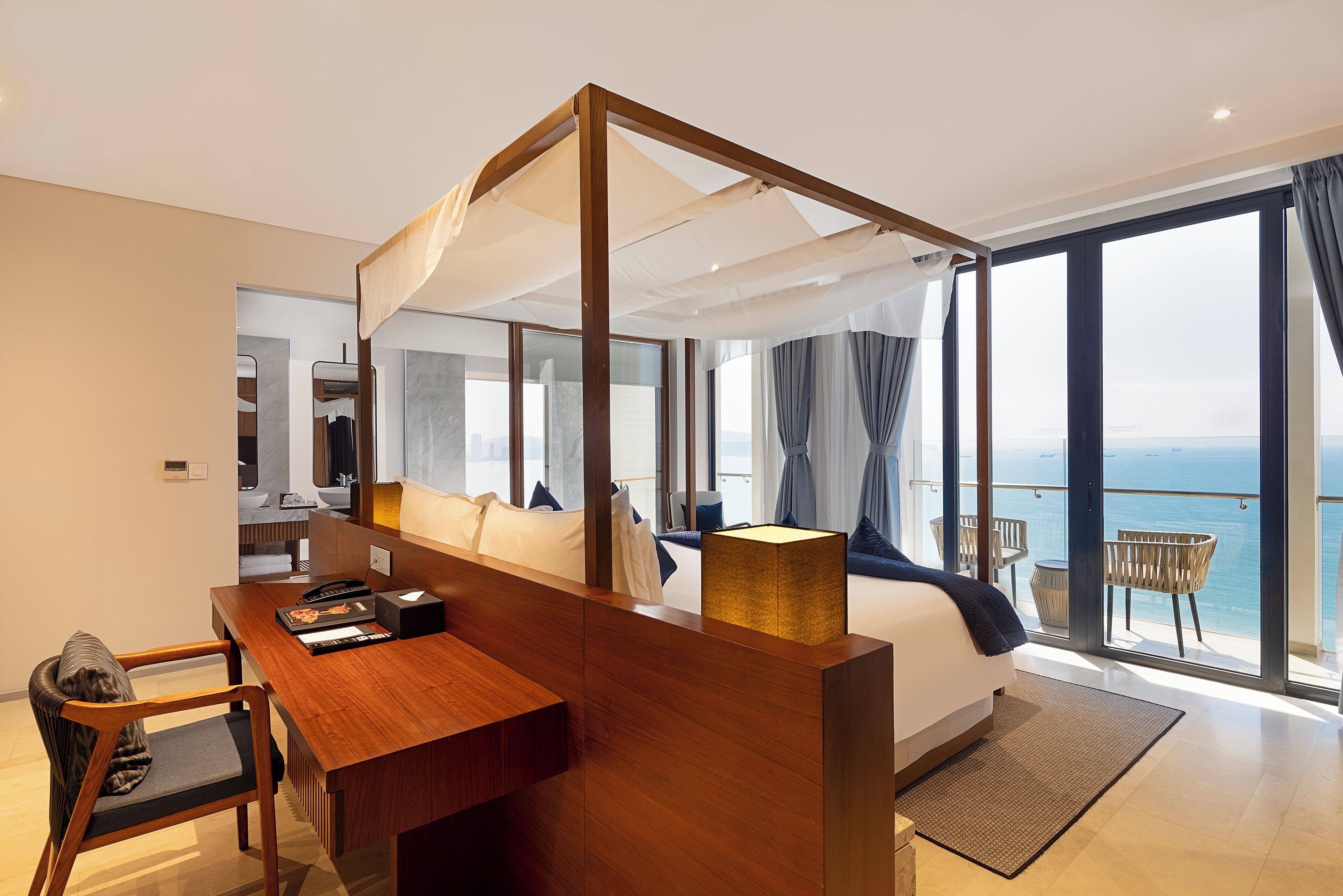 A modern hotel room with a large bed, a wooden desk, a laptop, and a view of the sea.