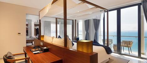 A modern hotel room with a large bed, a wooden desk, a laptop, and a view of the sea.