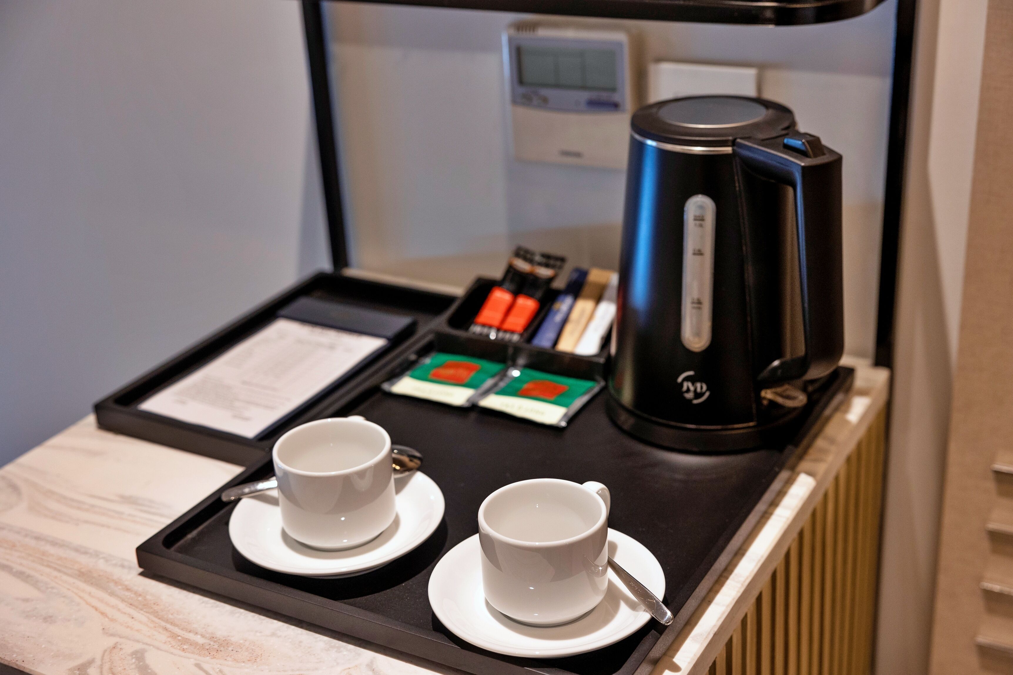 A tray with two white cups and saucers, a black electric kettle, and a tray of tea bags.