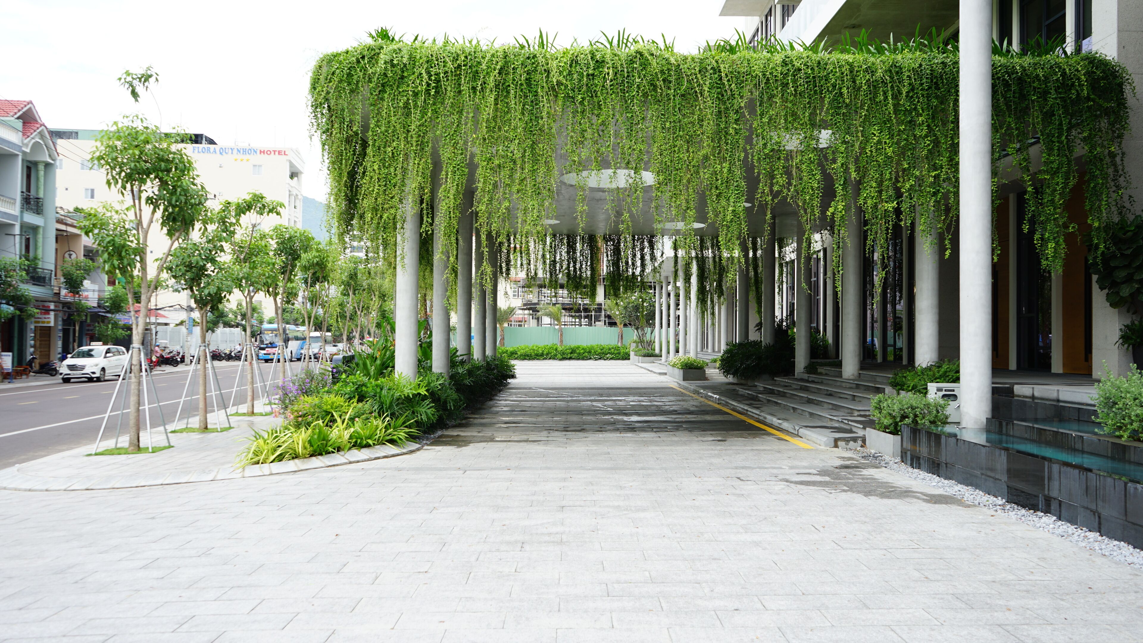 Una entrada de hotel con un paseo techado flanqueado por árboles y columnas.