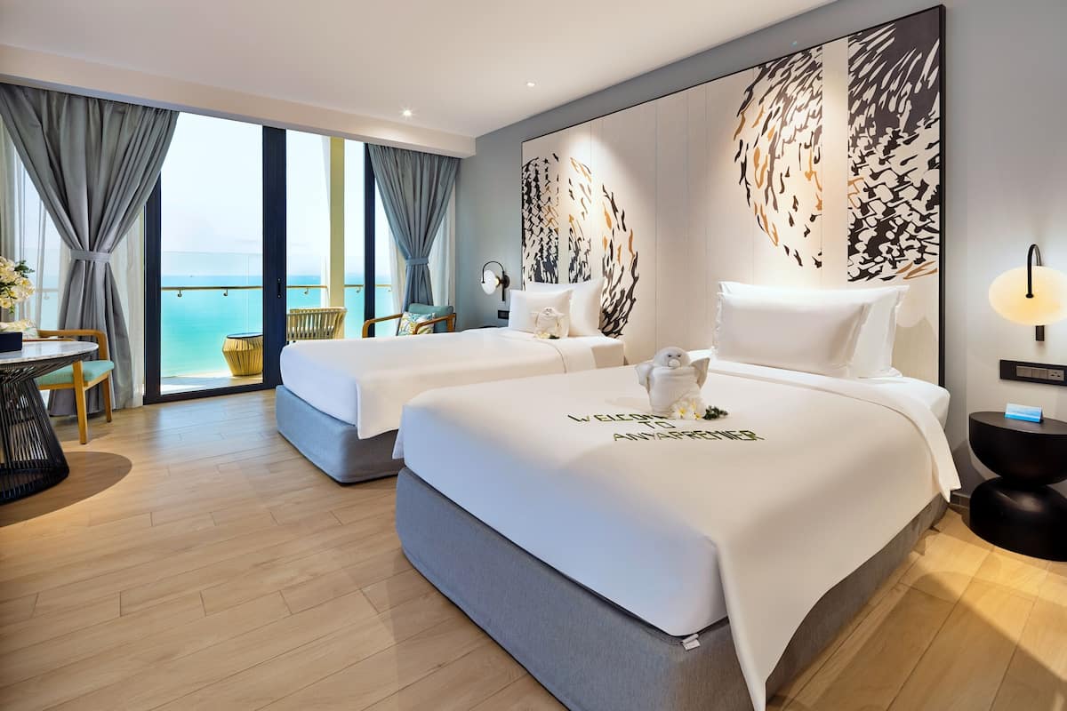 Ein modernes Hotelzimmer mit zwei Betten, einem Balkon mit Meerblick und einem großen, abstrakten Wandkunstwerk.