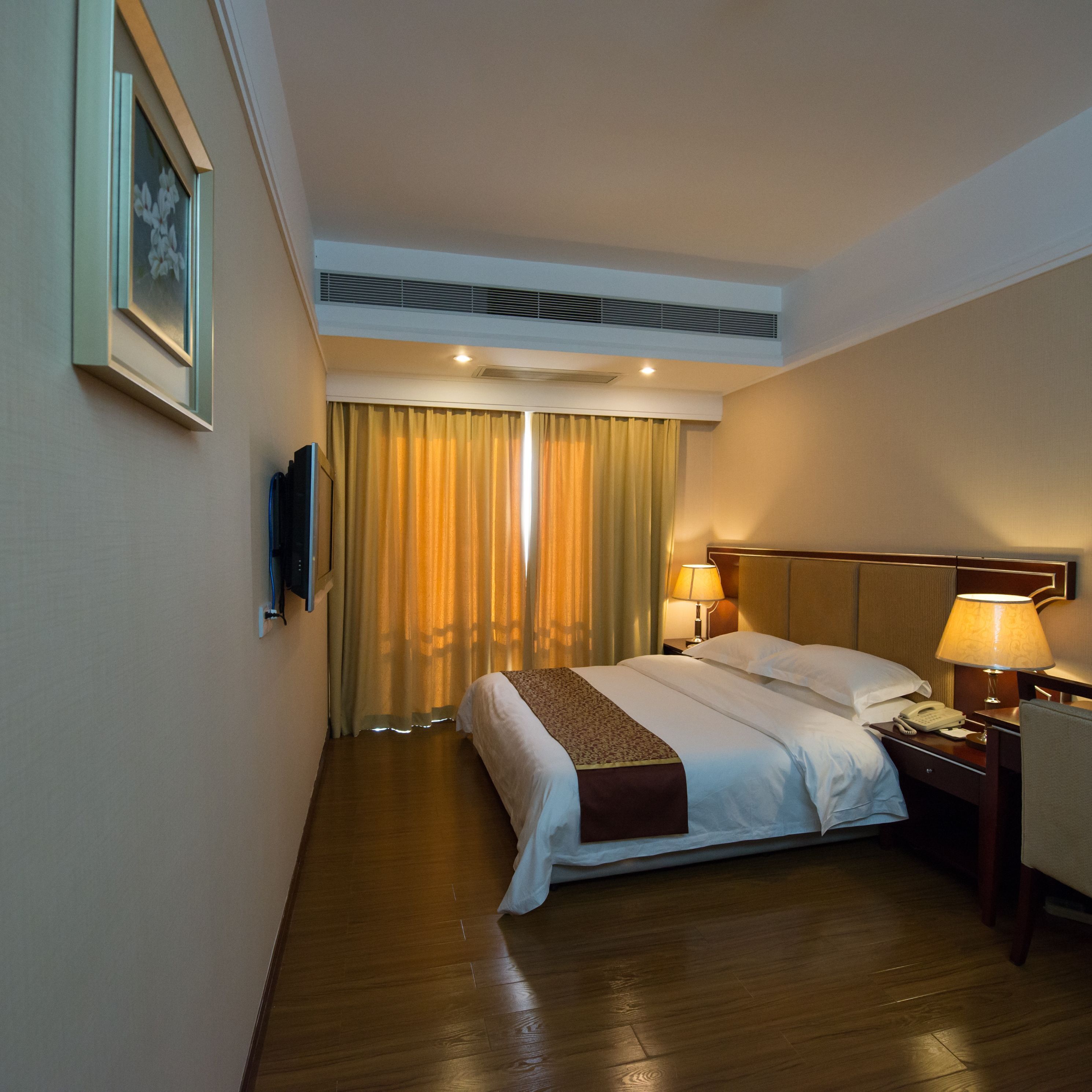 A hotel room with a bed, two bedside lamps, a telephone, and a television on the wall.