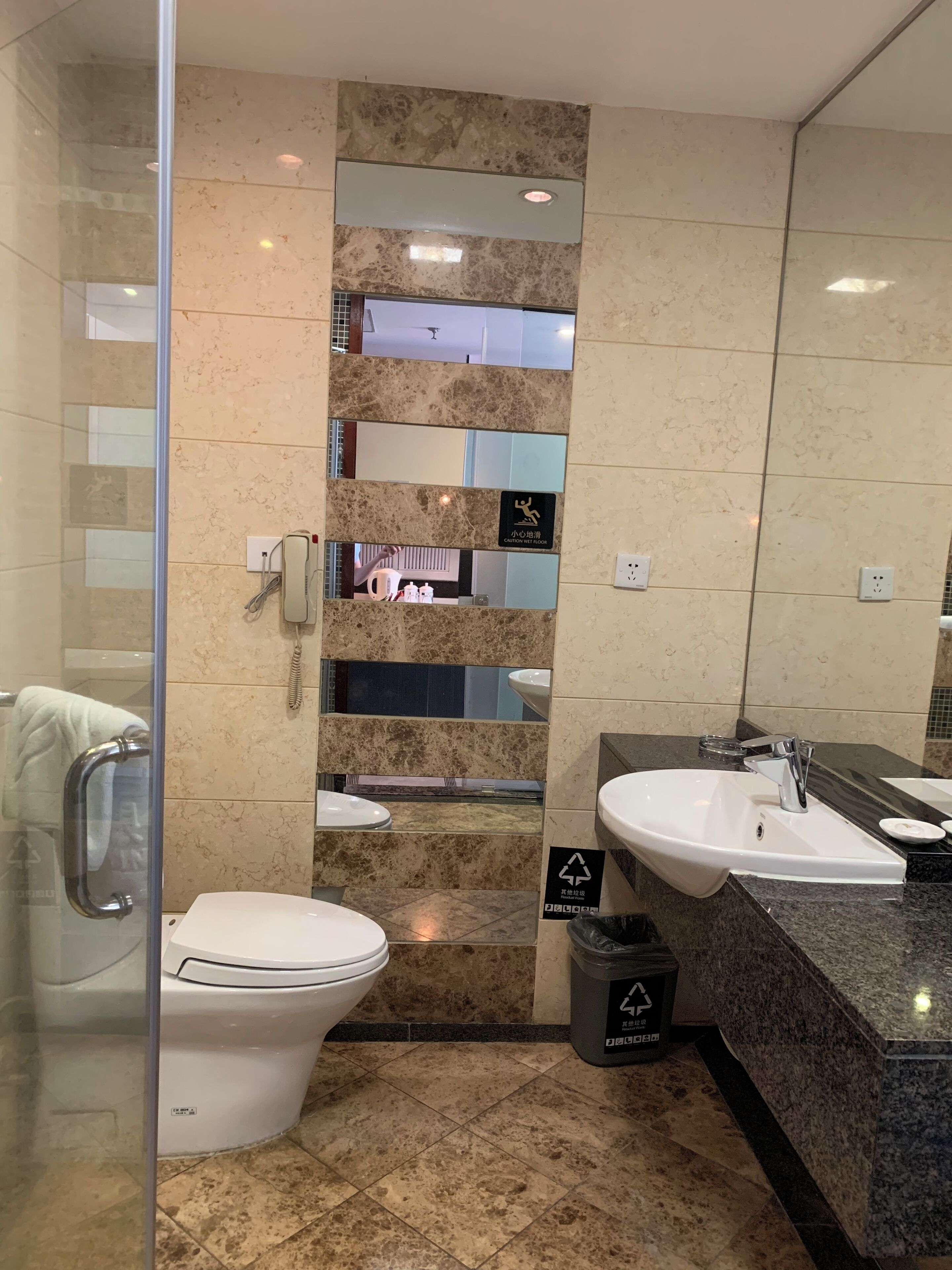 Uma casa de banho moderna com cabine de chuveiro em vidro, sanita branca, lavatório com espelho e um contentor de lixo.