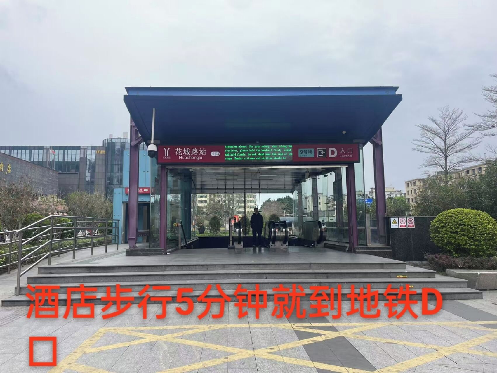 A modern building entrance with a glass facade, a sign indicating 'Entrance', and a digital display above the door.