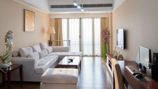 Una habitación de hotel moderna con sofá, reposapiés, escritorio y televisor.