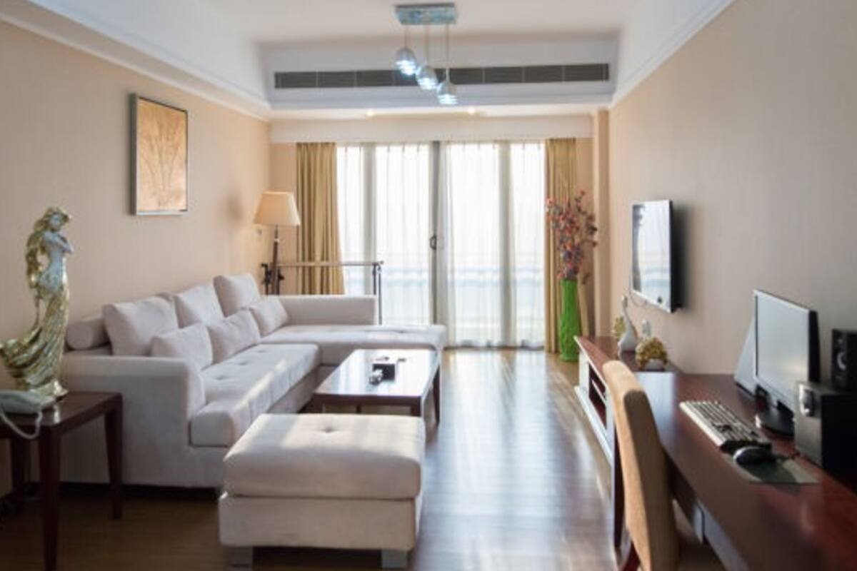 Una habitación de hotel moderna con sofá, reposapiés, escritorio y televisor.