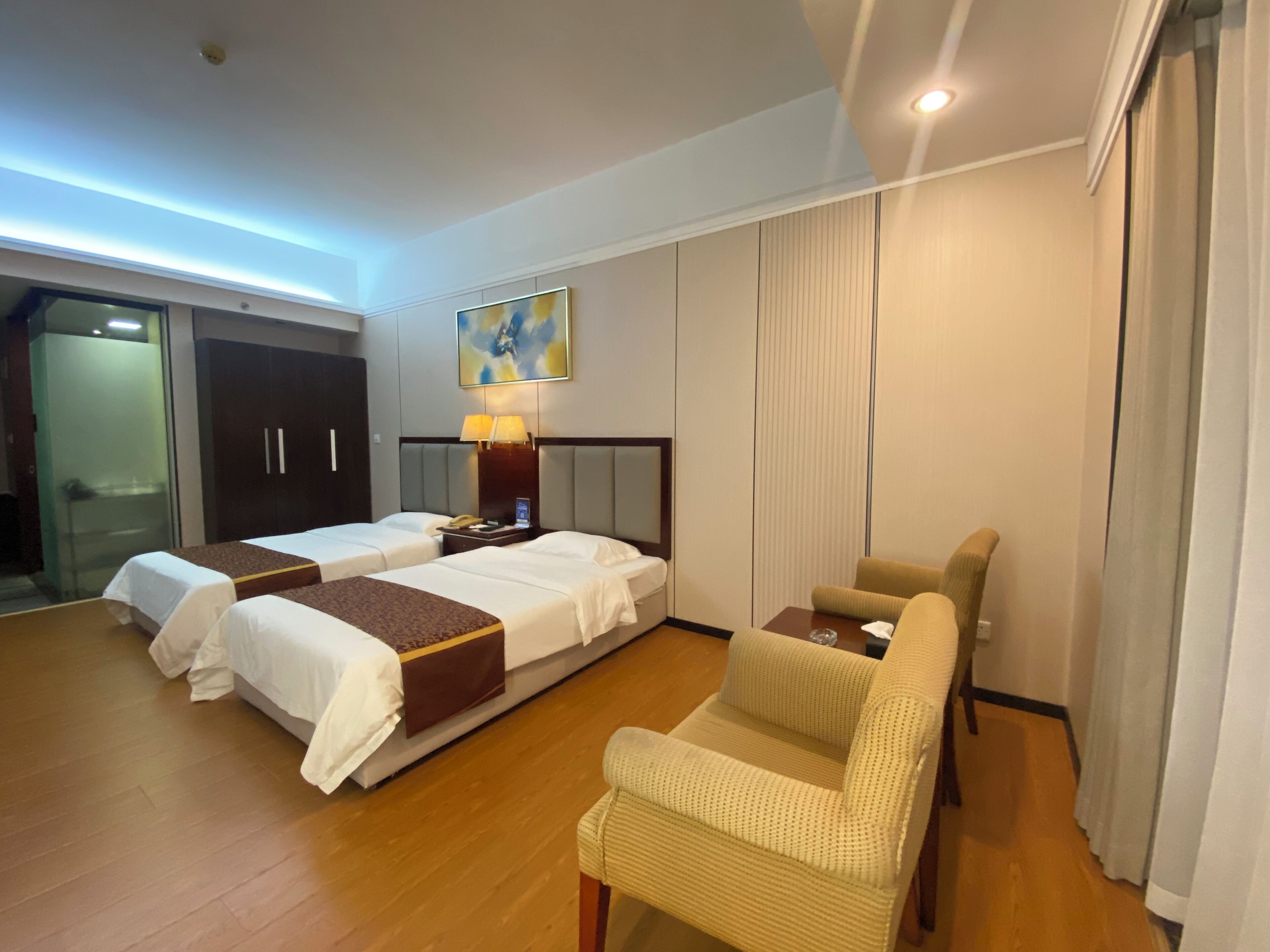 Ein Hotelzimmer mit zwei Betten, einem Sofa, einem Schreibtisch, einer Lampe und einem Bild an der Wand.